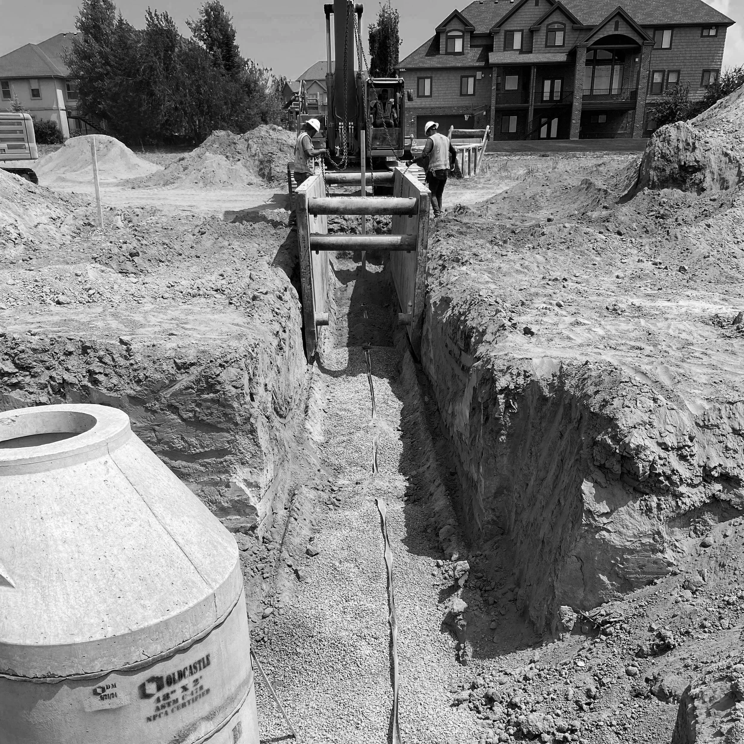 black and white photo at alpine heights civil engineering project of two mean and tractor digging trench
