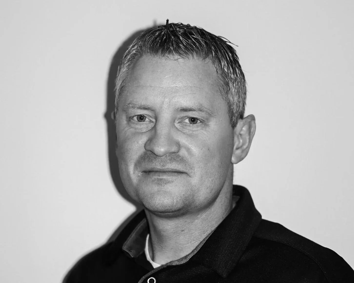 Black and white photo of a smiling man with spiked hair, wearing a dark collared shirt. Blake Jolley owner of Connect Engineering and Surveying