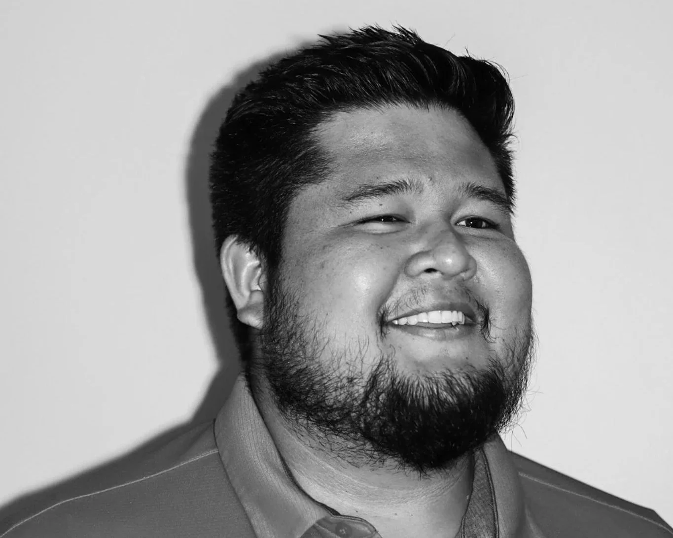 Black and white photo of a smiling man with a beard and short hair, wearing a collared shirt, against a plain background. A Connect Engineering Employee.