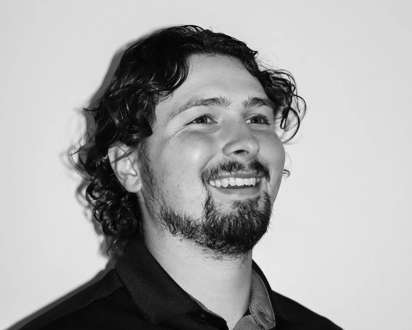 Black and white portrait of a man with curly hair and a beard, smiling and looking slightly to his right. A Connect Engineering Employee.
