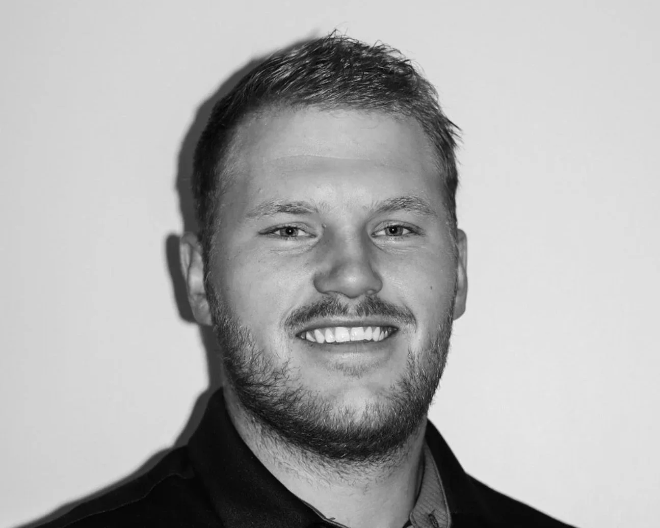 Black and white portrait of a young man smiling. A Connect Engineering Employee.