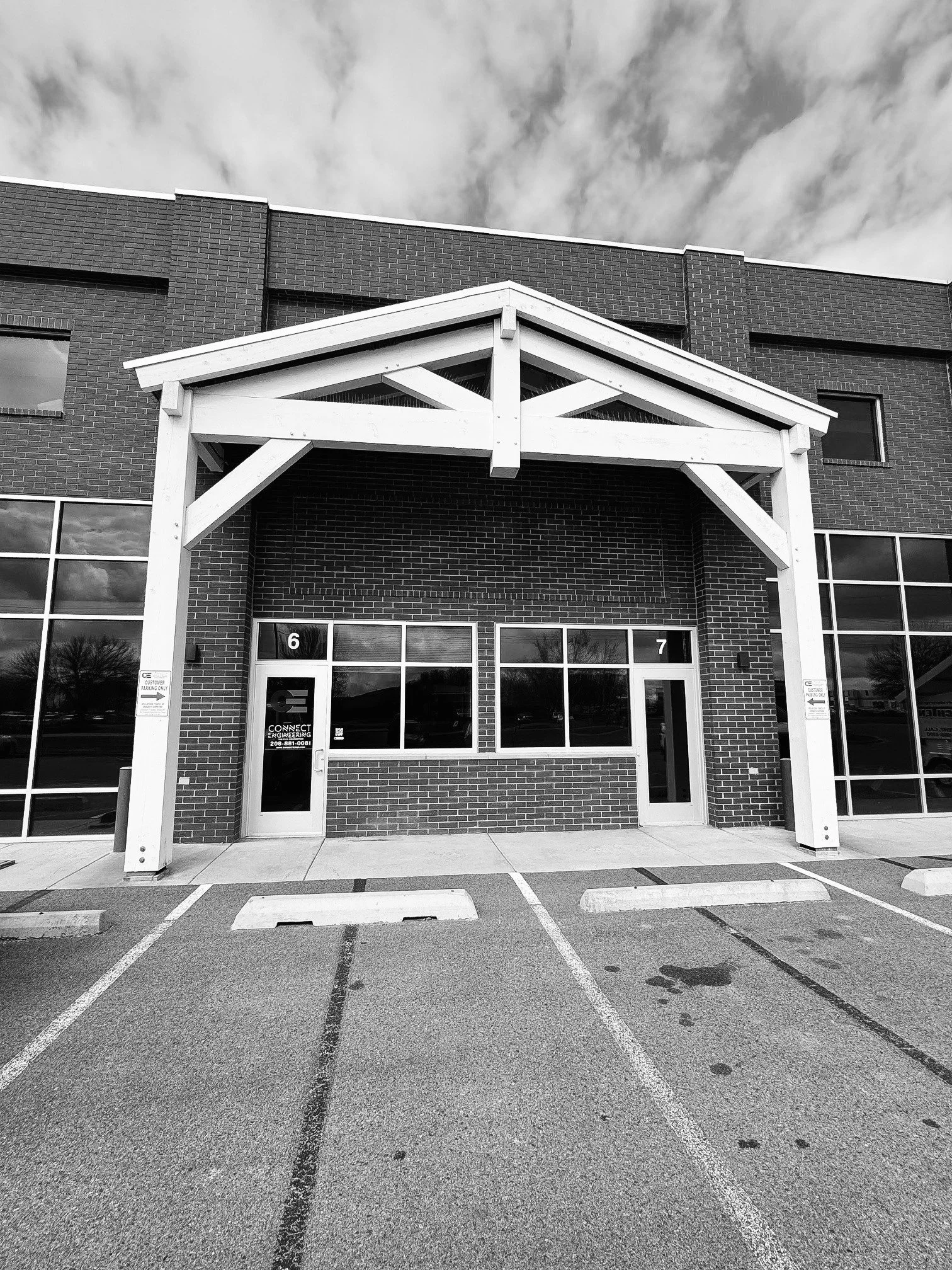 Black and white photo of a commercial building with two front entrances featuring large windows, brick and siding exterior, and a white wooden awning structure over the entrances. Front doors of Connect Engineering office in Idaho Falls Idaho.
