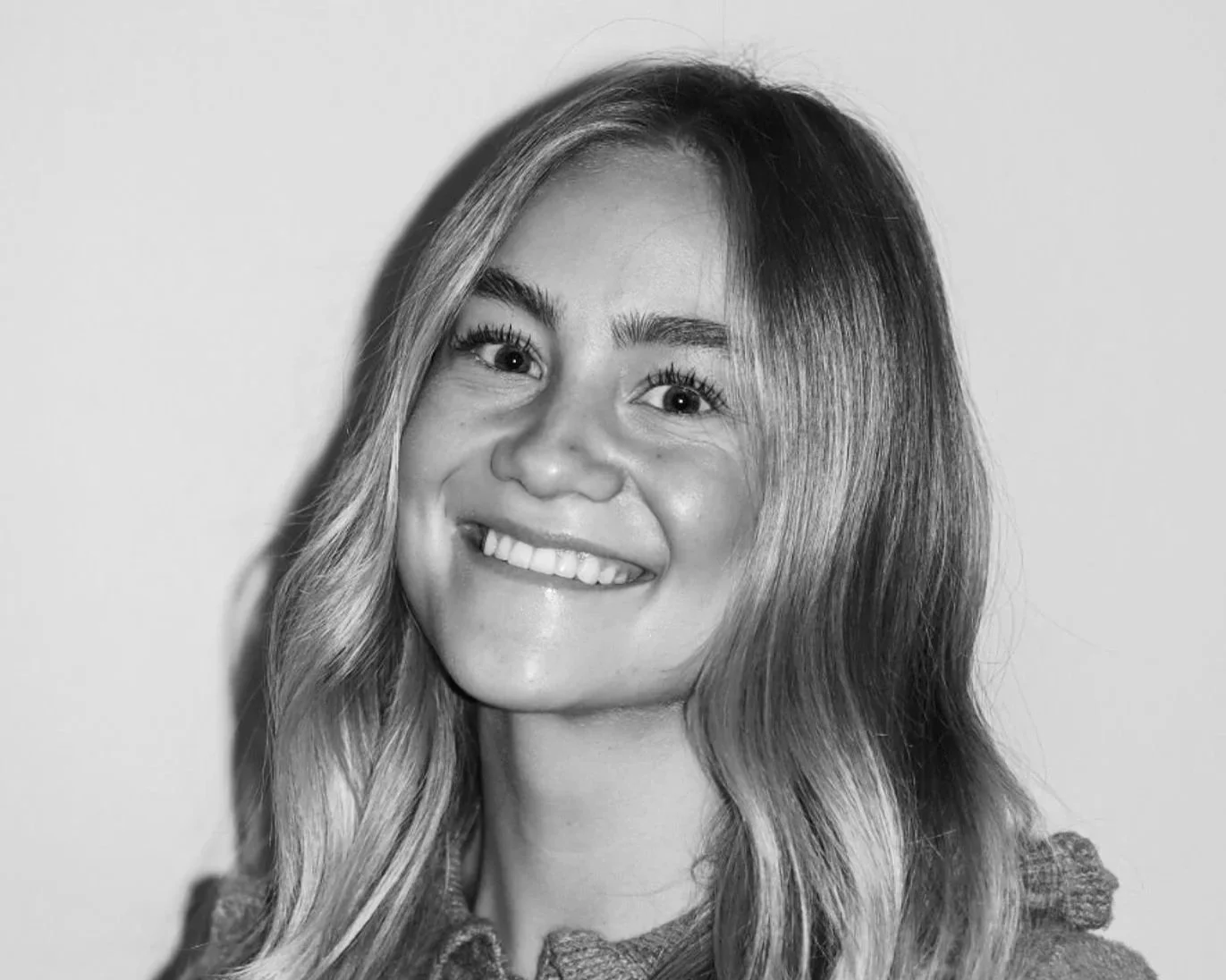 Black and white photo of a smiling woman with long wavy hair wearing a button-up sweater. A Connect Engineering Employee.