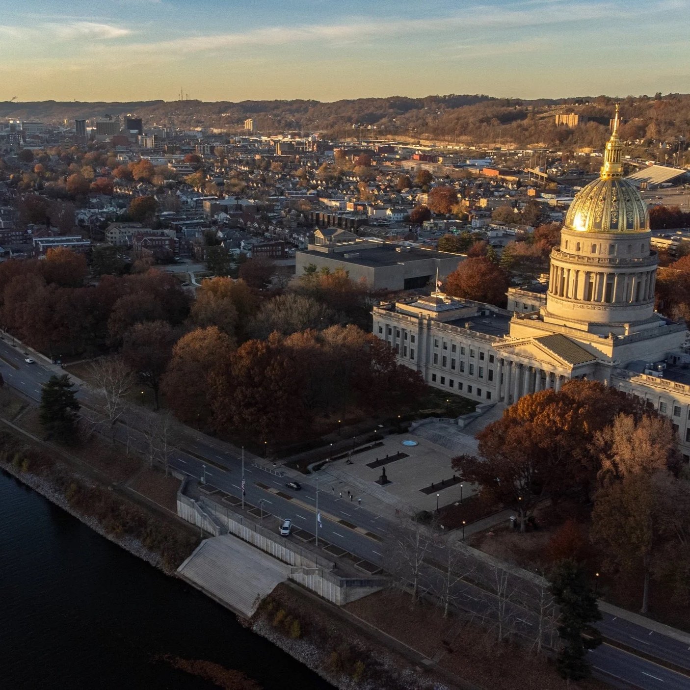 Aerial view of a cityscape featuring the Tennessee State Capitol building with a golden dome, surrounded by trees in fall colors, and a nearby road along a river.