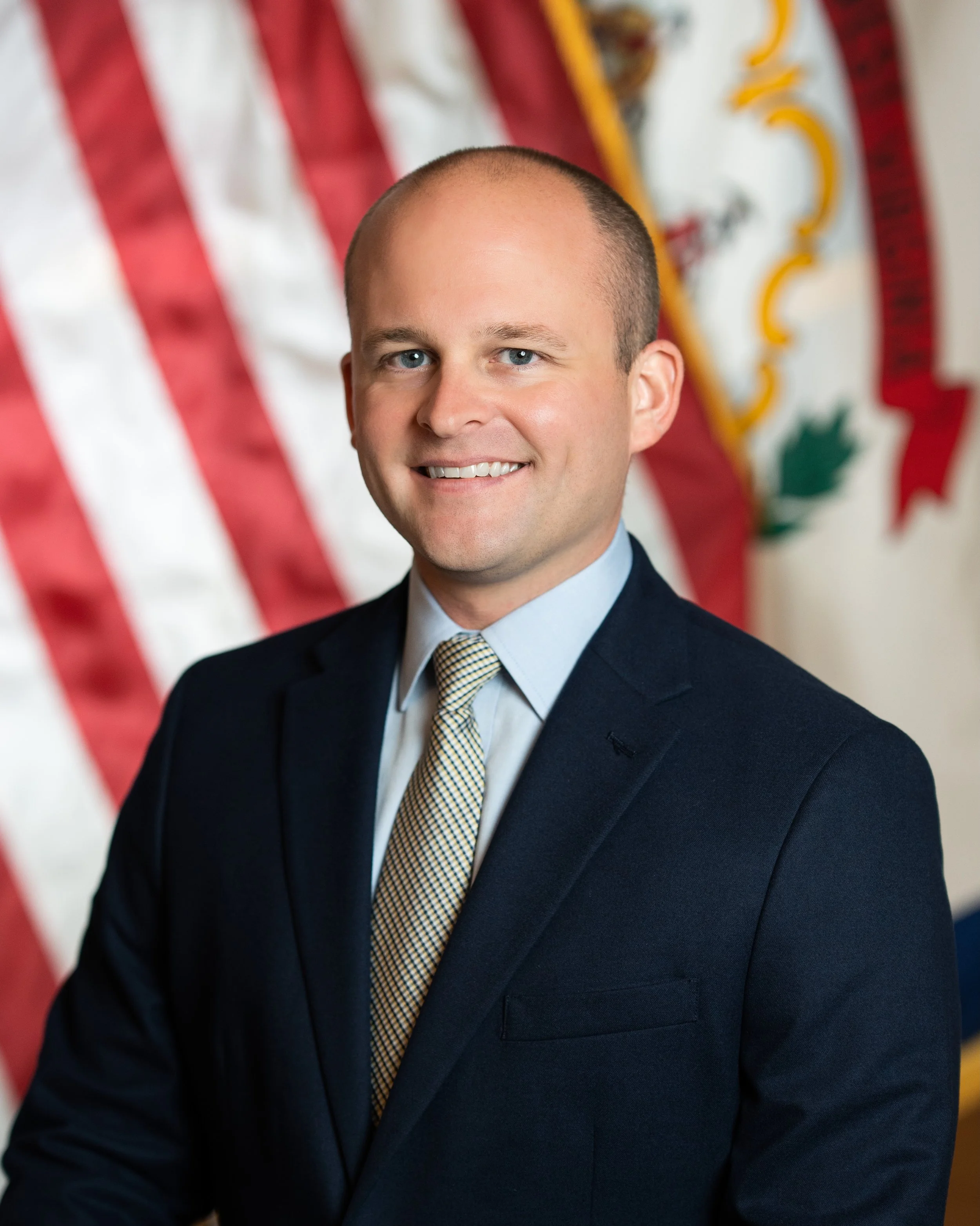 Man in formal suit standing in front of American and state flags