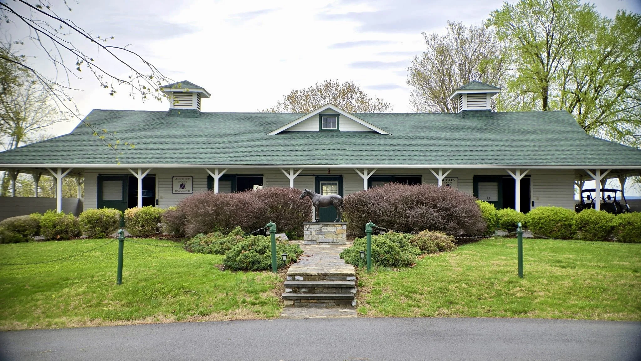 An Audley Farm facility for equine activities, with signs indicating "Audley Farm Equine". The statue of Sir Barton sits regally in front of the facility.