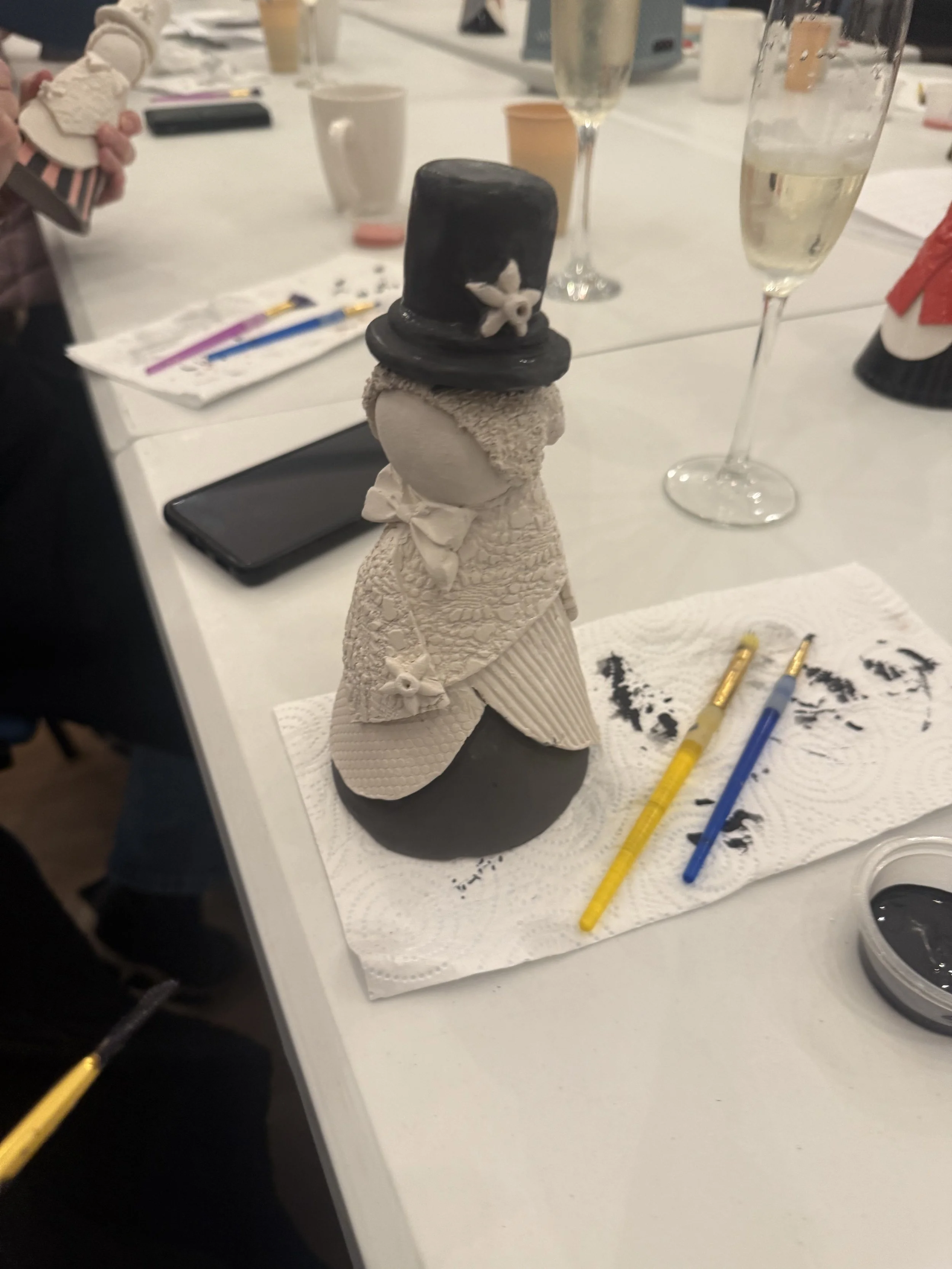 A decorative figure resembling a snowman with a black top hat, bow tie, and beige textured clothing, standing on a white paper towel.