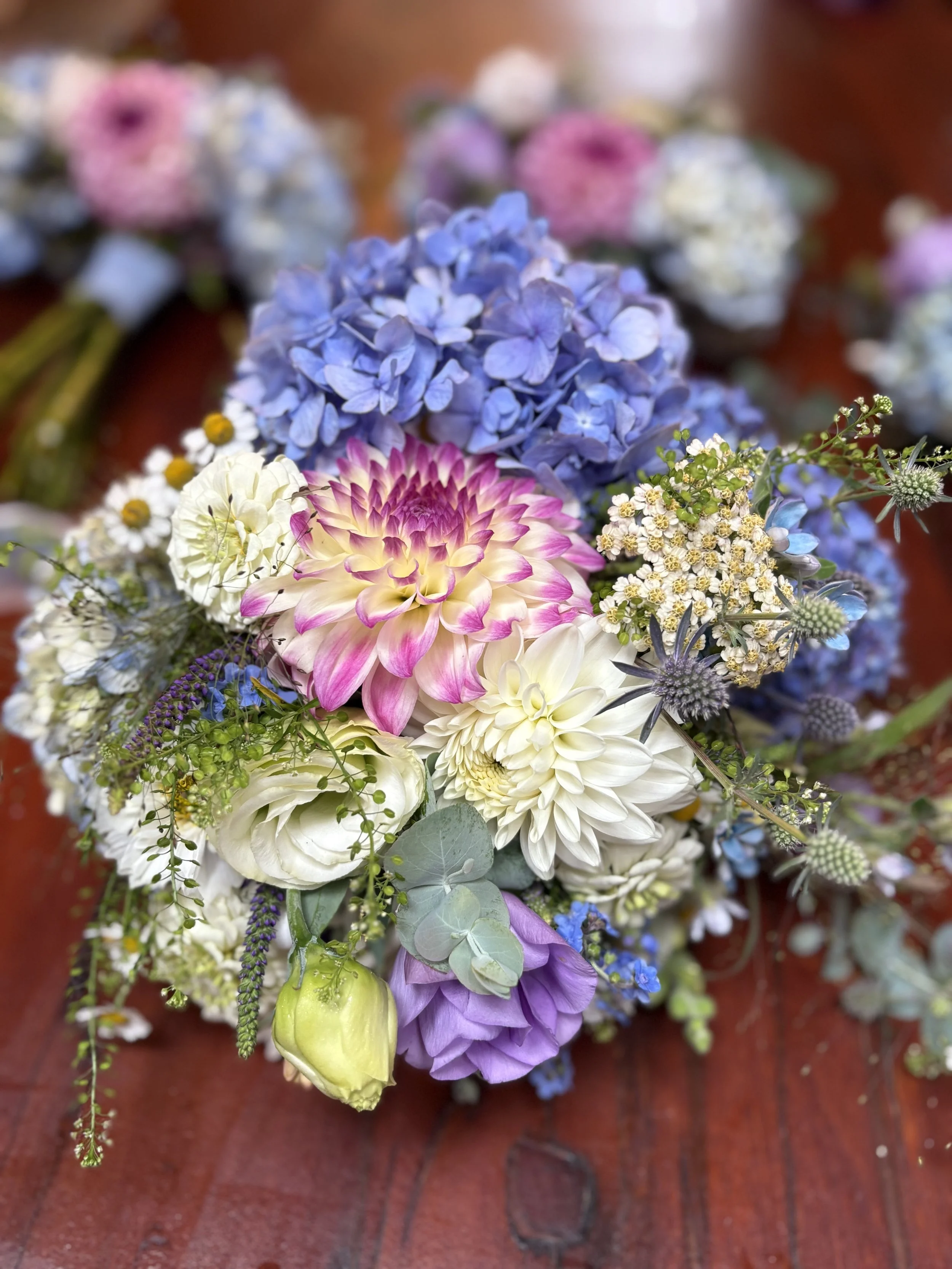 Colorful bouquet of various flowers including pink, white, purple, and blue blooms on a wooden surface.