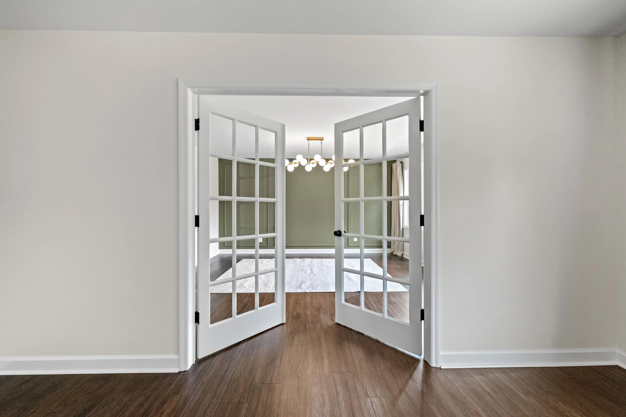 Open white French doors leading into a bright living room with a chandelier and green walls.