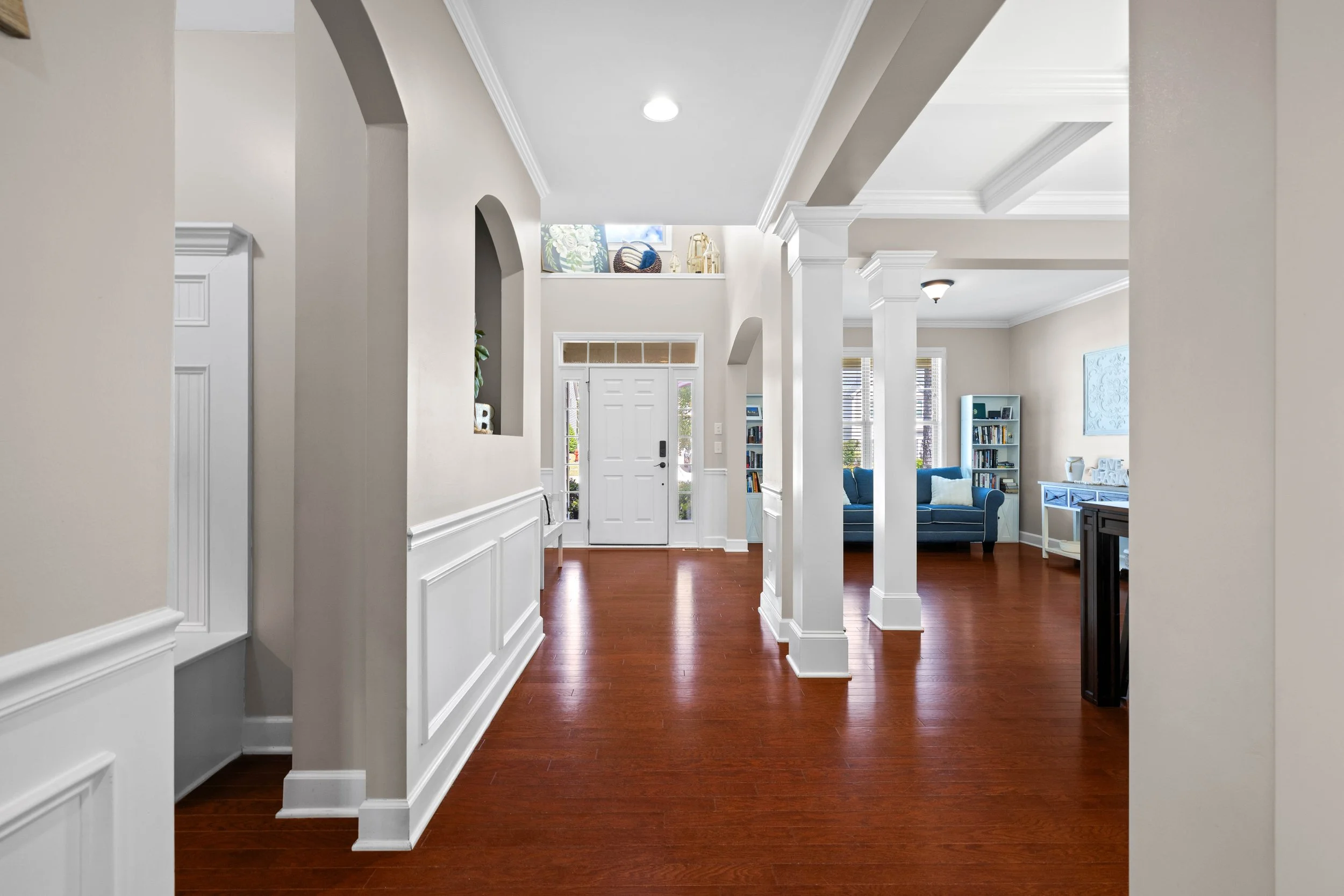 View of a bright foyer and living room in a house with hardwood floors, white walls, and various furniture and decor items.
