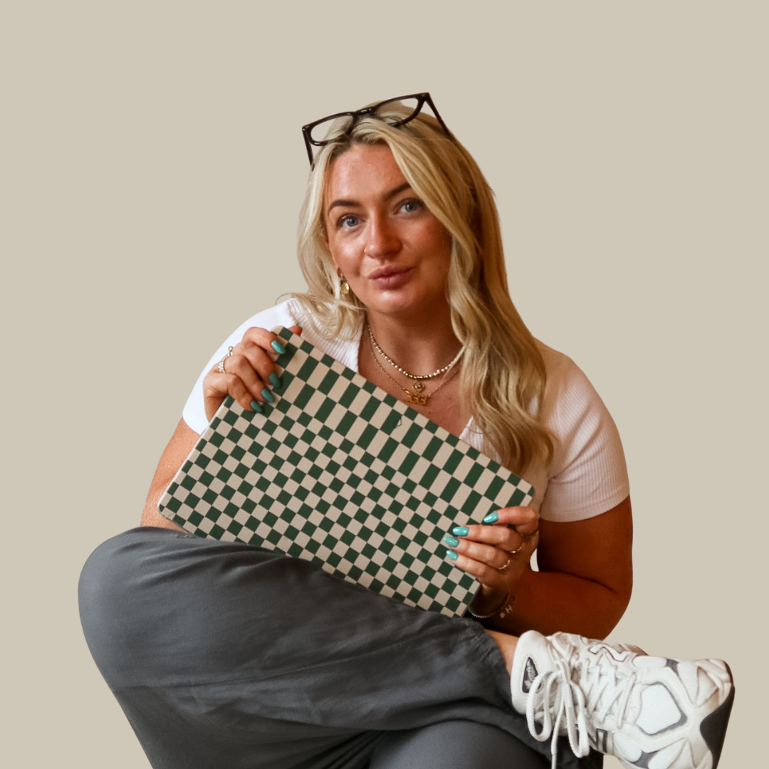 Close-up of a young woman with long blonde hair, blue eyes, wearing a white off-shoulder top, gold necklace, and earrings, against a plain beige background.