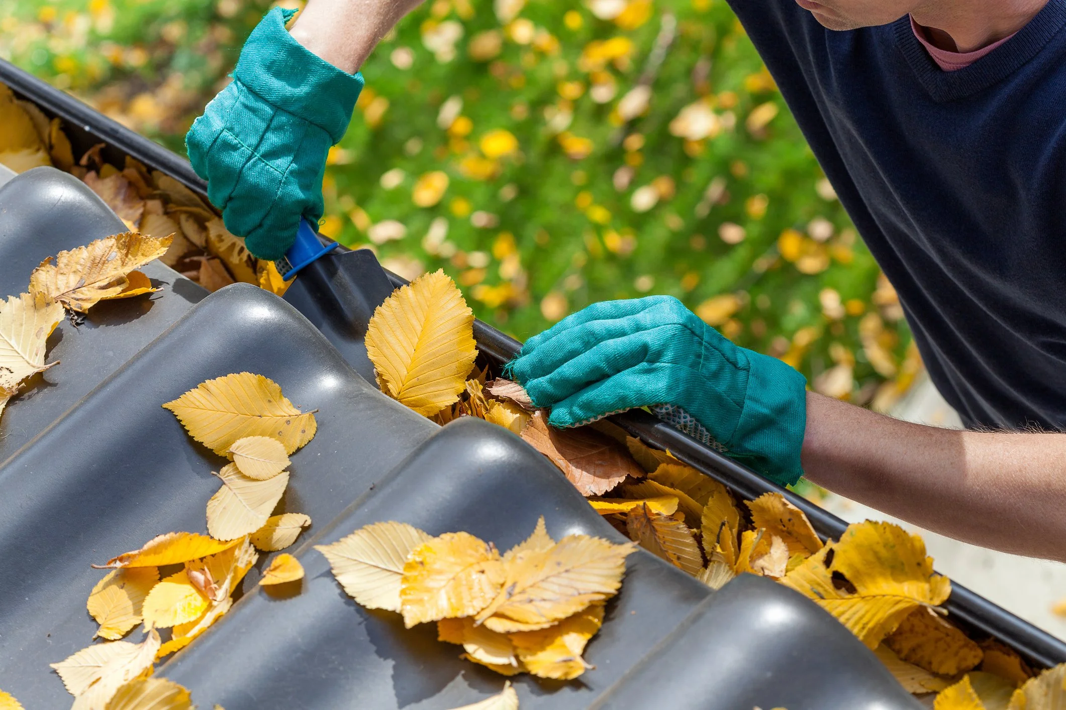 A person gutter cleaning in Omaha, Nebraska with many leaves inside the gutter.
