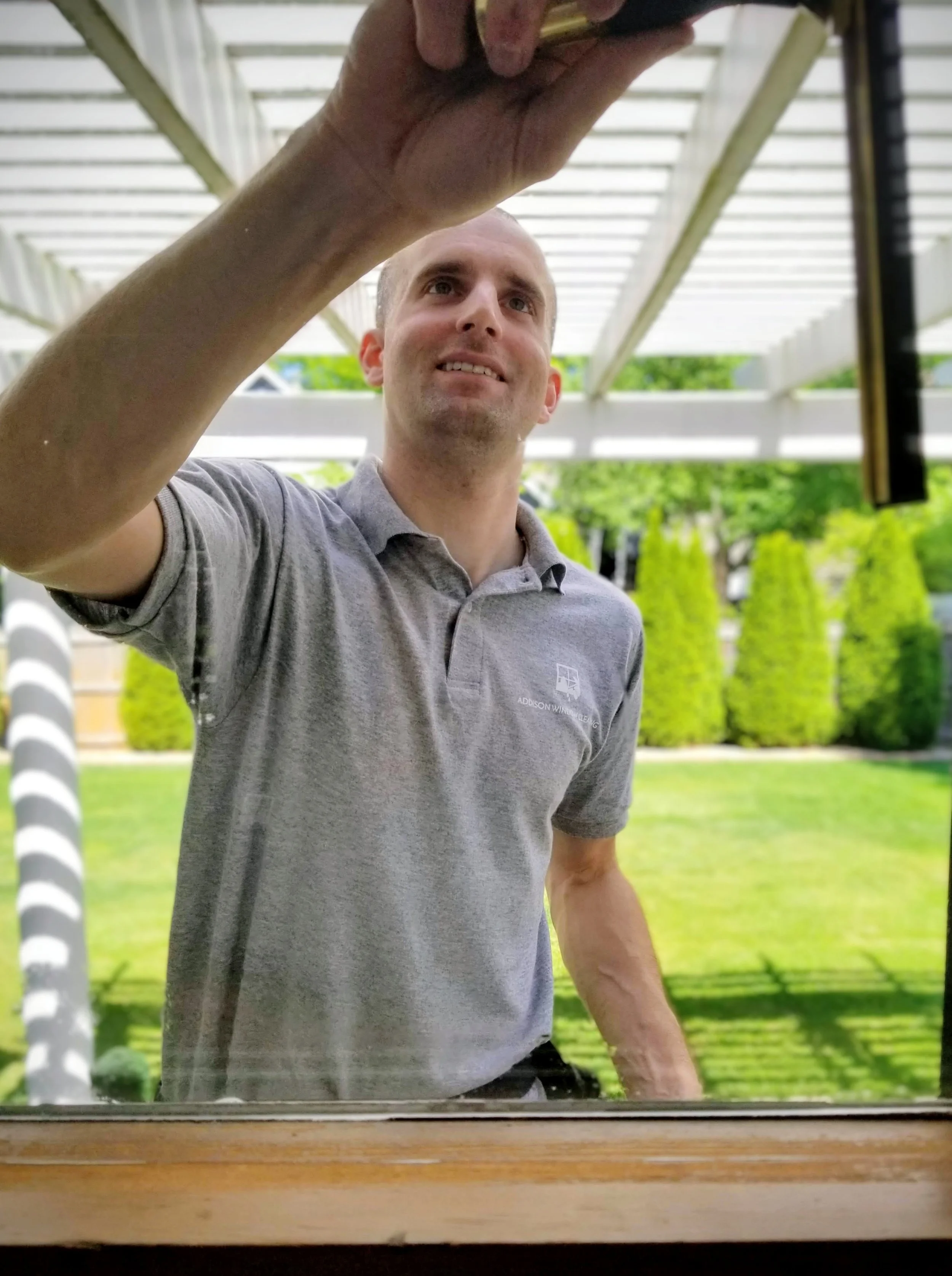 A man in a gray polo shirt is cleaning windows with a squeegee in Omaha, Nebraska.