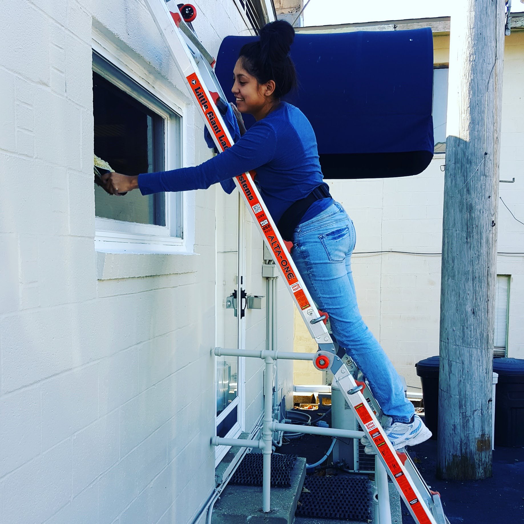 A woman standing on an extension ladder is cleaning a window of a commercial building in Omaha, Nebraska.