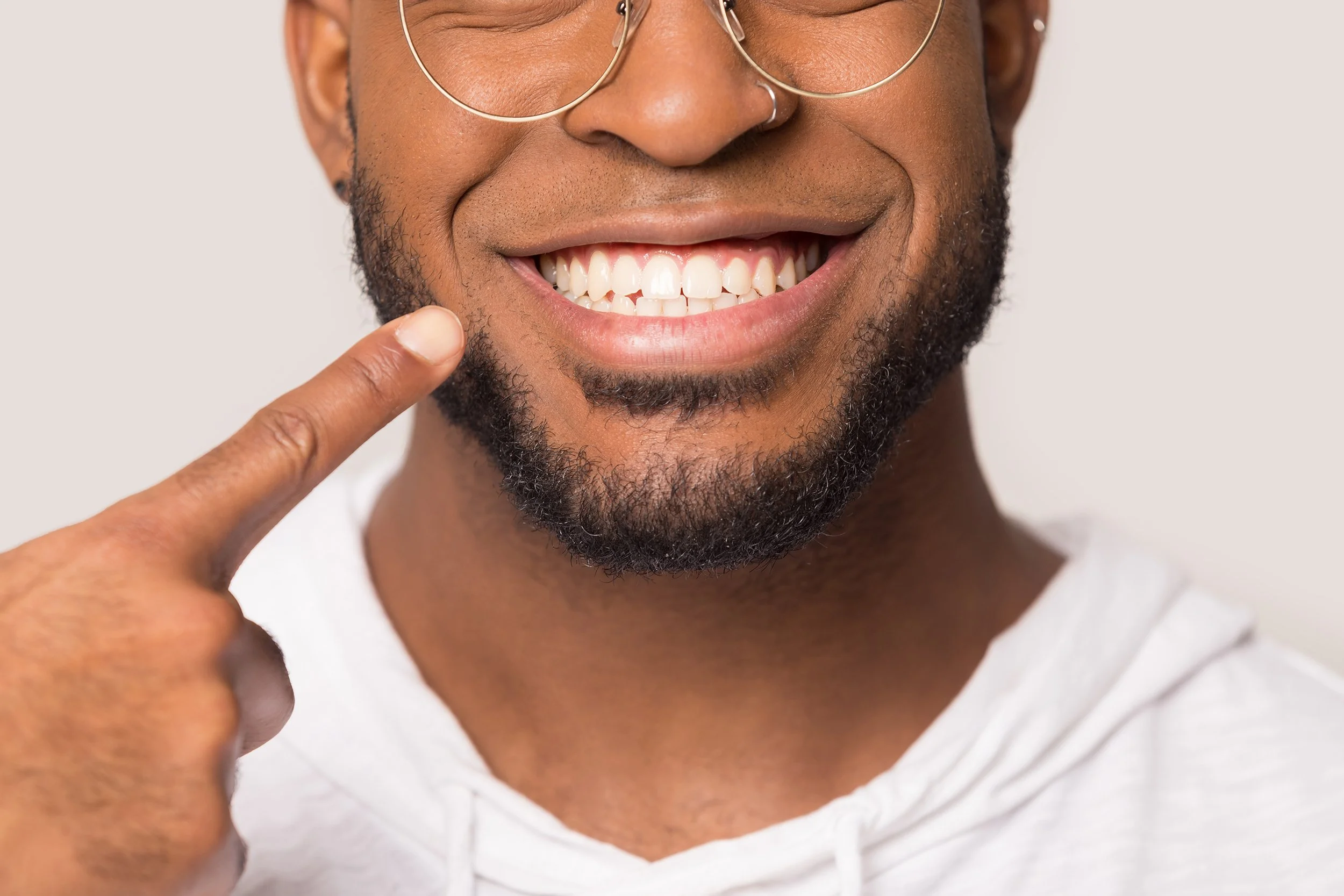 A man points to his new smile. When researching dental crown pricing, costs vary significantly based on materials and complexity.  Learn more in our completed guide on dental crown pricing.