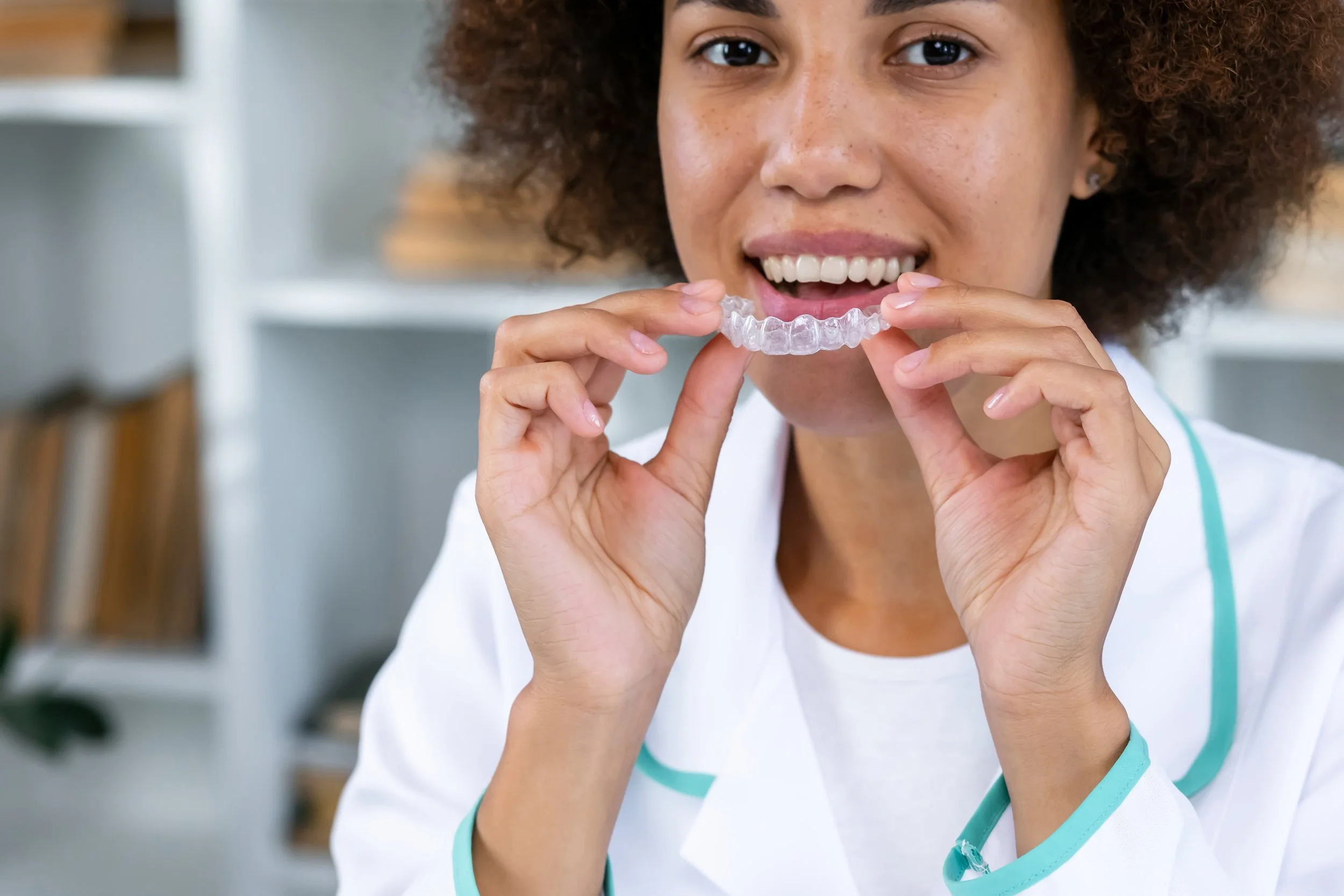 Woman holding clear aligners near her mouth. Clear aligners are effective for the right cases — but results depend on more than the technology. Here's what every patient should know before starting treatment.