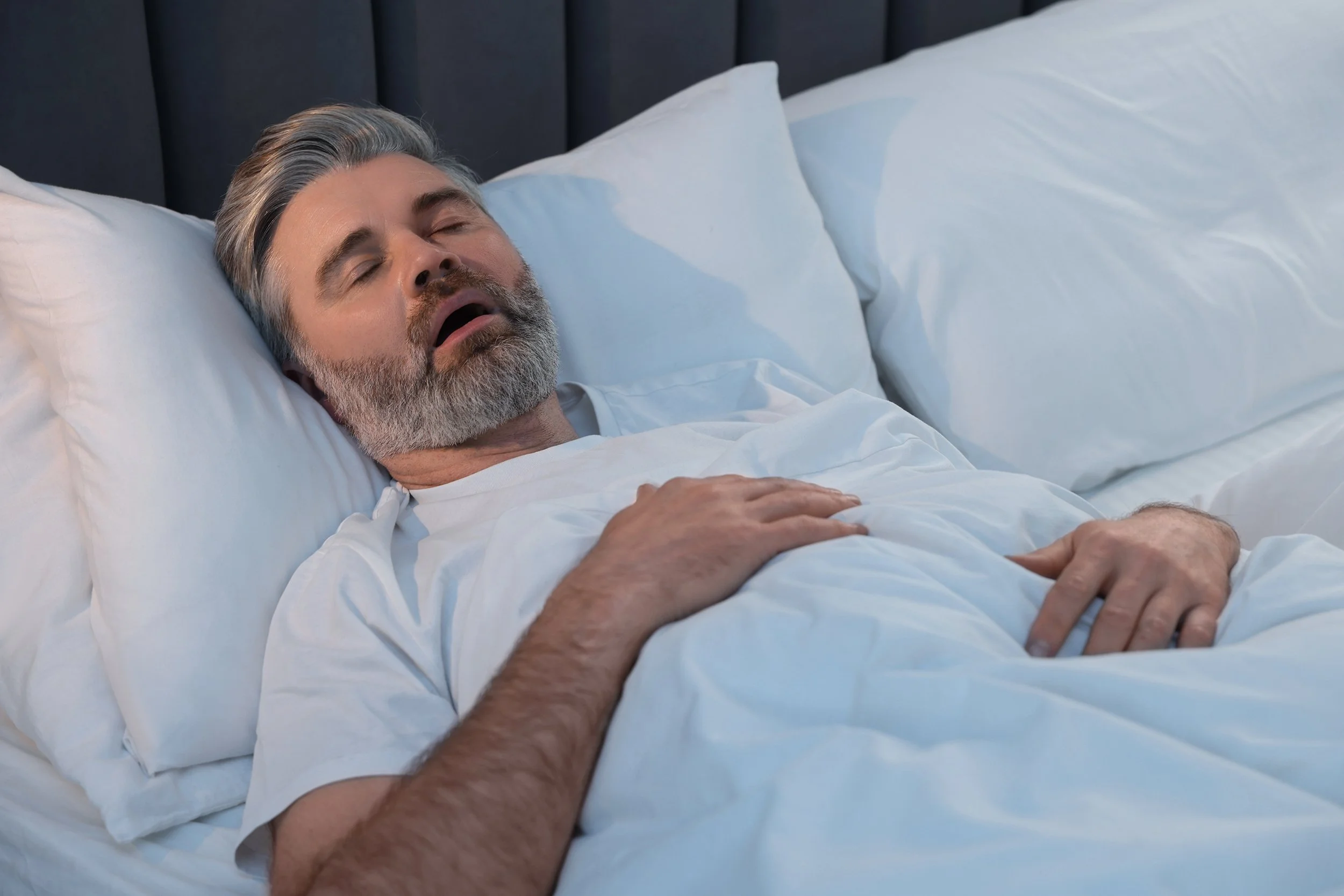 A man snores in bed. Discover how oral appliances for snoring can end sleepless nights. Learn about custom devices, costs, effectiveness, and whether this solution is right for you.