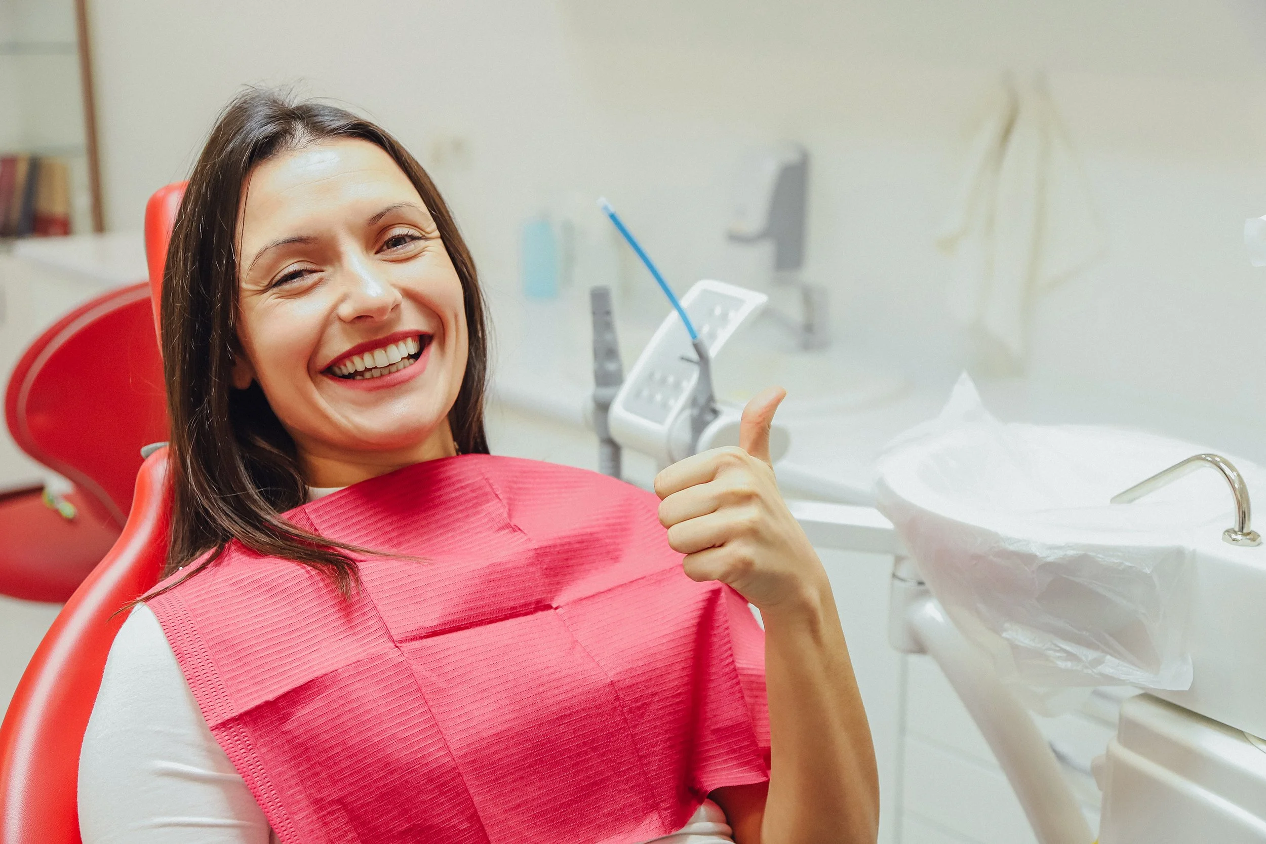 A woman smiles in a dental chair. Learn more about minimally invasive dentistry and how it helps the overall health of your smile.