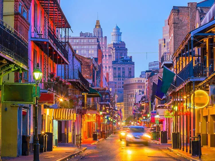 Colorful city street in the evening with buildings, neon lights, and a blurred car moving through.