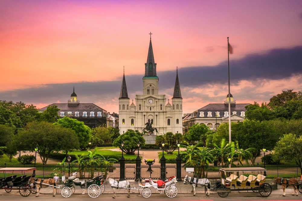 Jackson Square in New Orleans with St. Louis Cathedral, horse-drawn carriages, and a vibrant sunset in the sky.