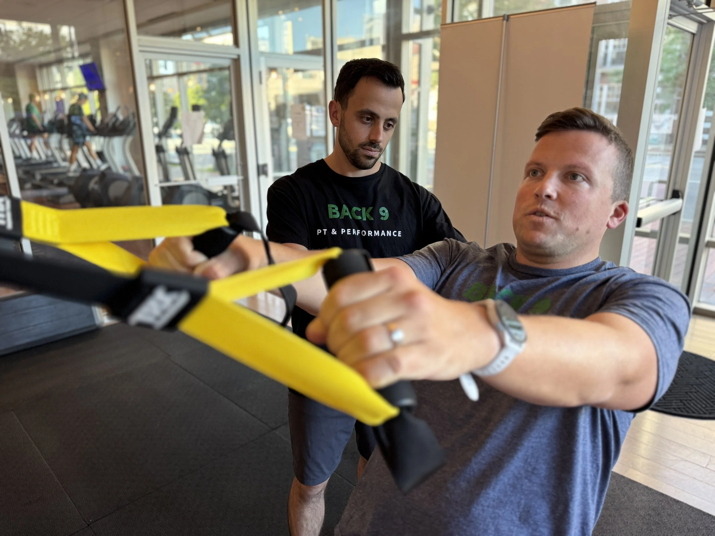 Physical therapist supervising a client doing back exercises with suspension training straps in Cambridge, MA