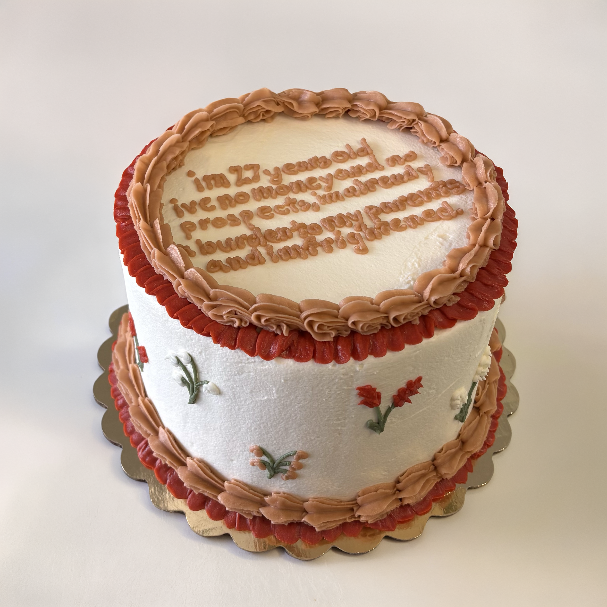 A decorated birthday cake with white icing, pink frosting accents, and floral decorations, with message written in pink frosting on top.