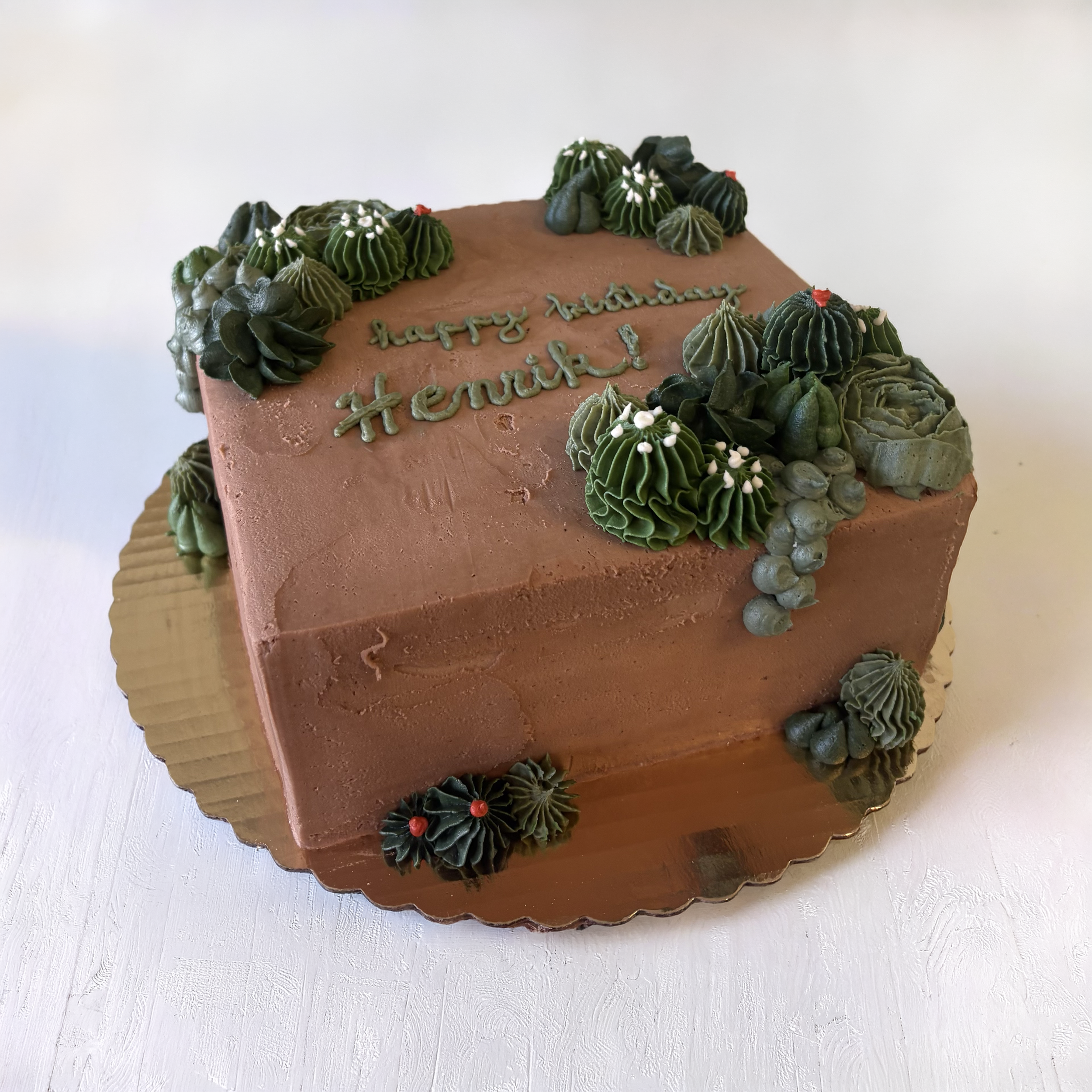 Chocolate birthday cake decorated with green and black piped icing, floral designs, and a "happy birthday Henrik" message on top.