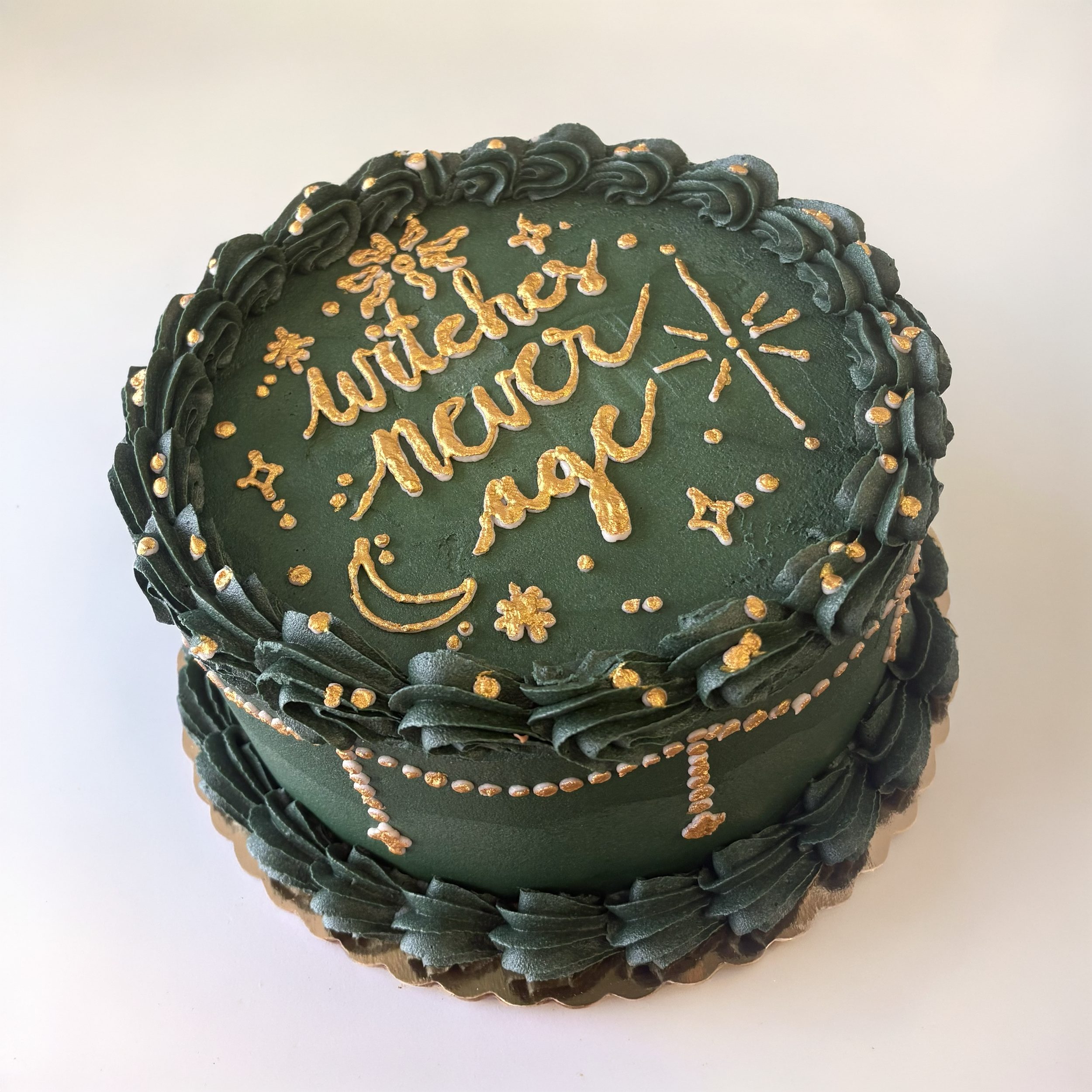 Close-up of a decorated green cake with gold accents and the word 'Merry Christmas' written on it, surrounded by small star and snowflake decorations.
