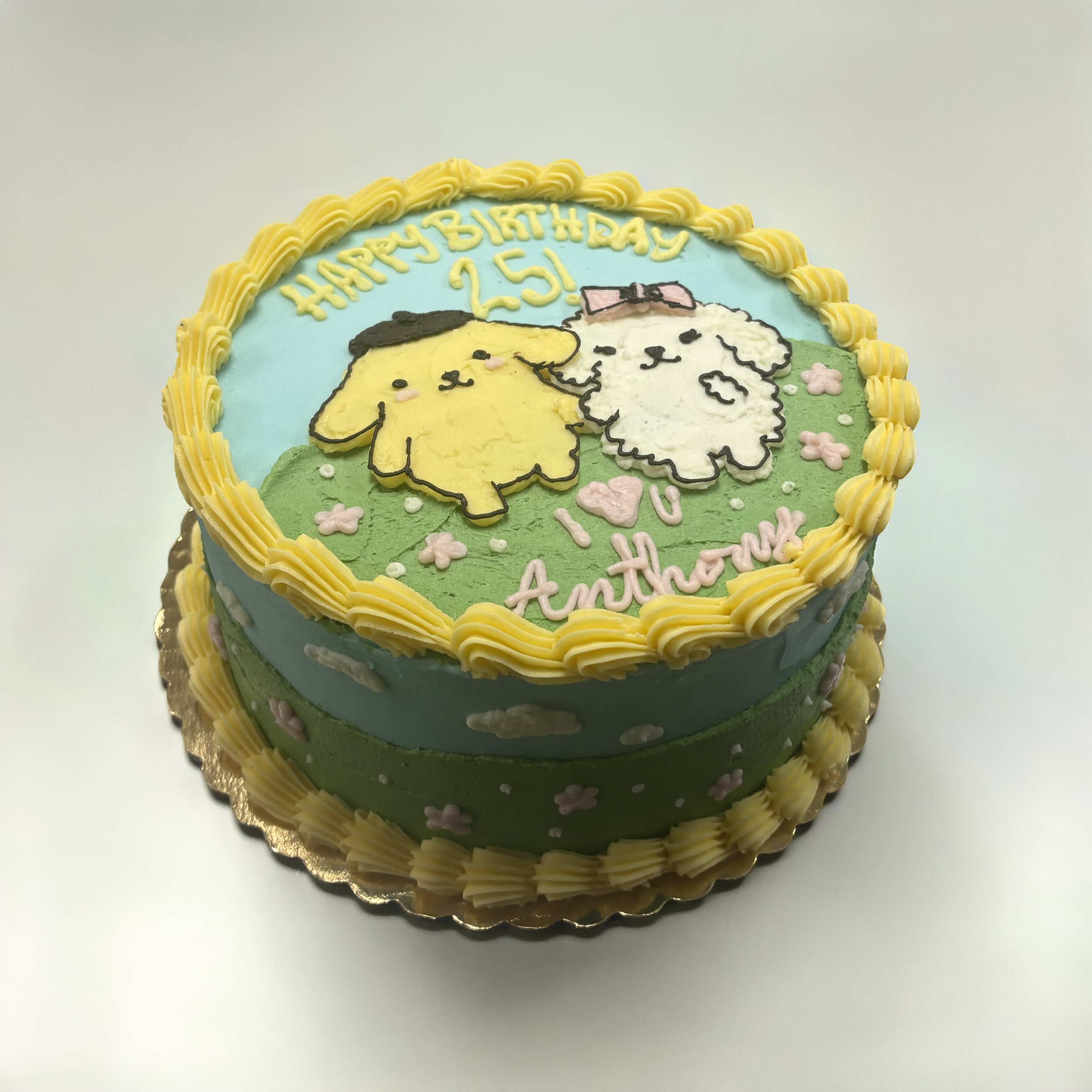 Decorative birthday cake with yellow, white, and green icing, featuring cartoon characters, flowers, and the text "Happy Birthday 25!" with yellow piping around the edges.