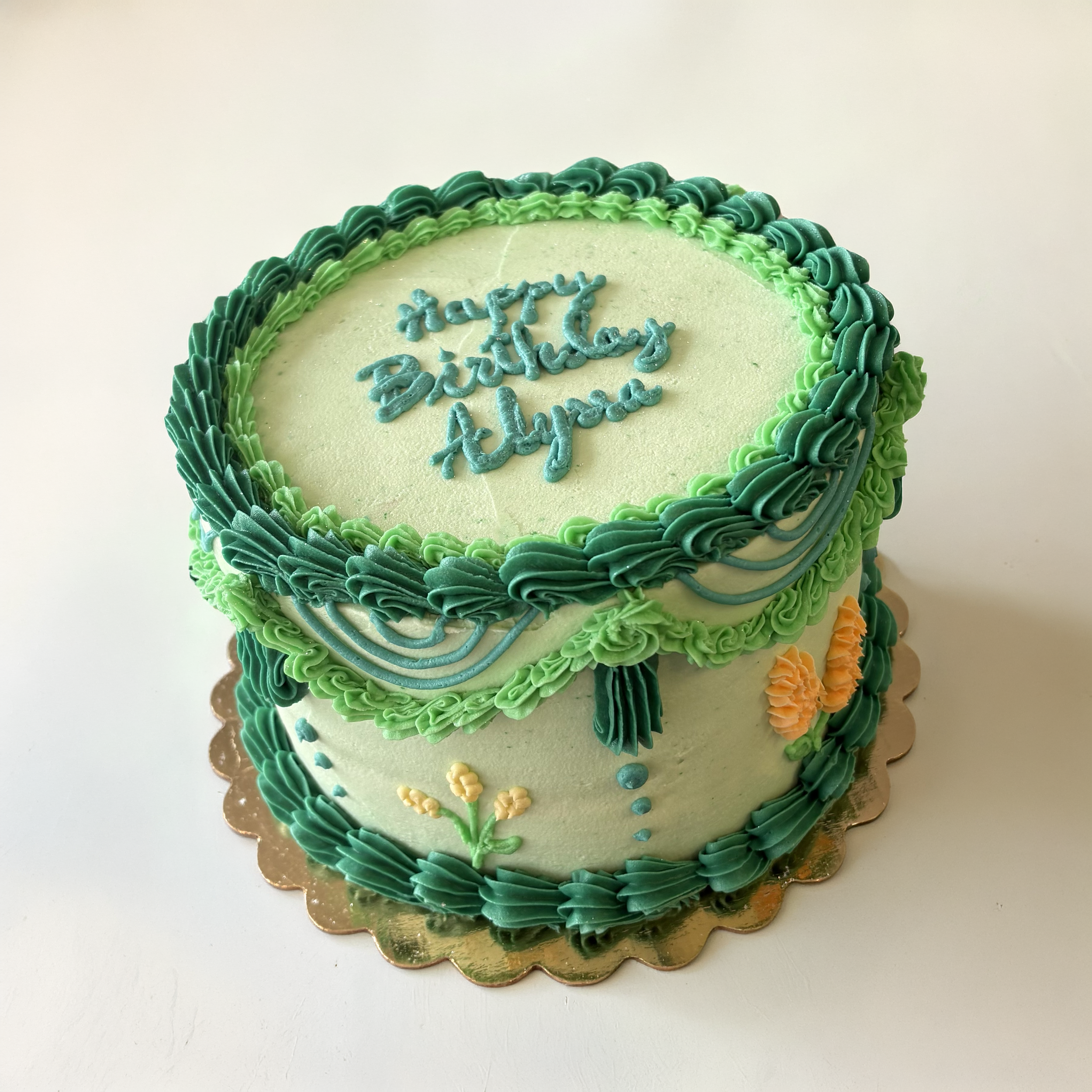 Decorated birthday cake with green, blue, and yellow frosting, and a message written in blue frosting on top.
