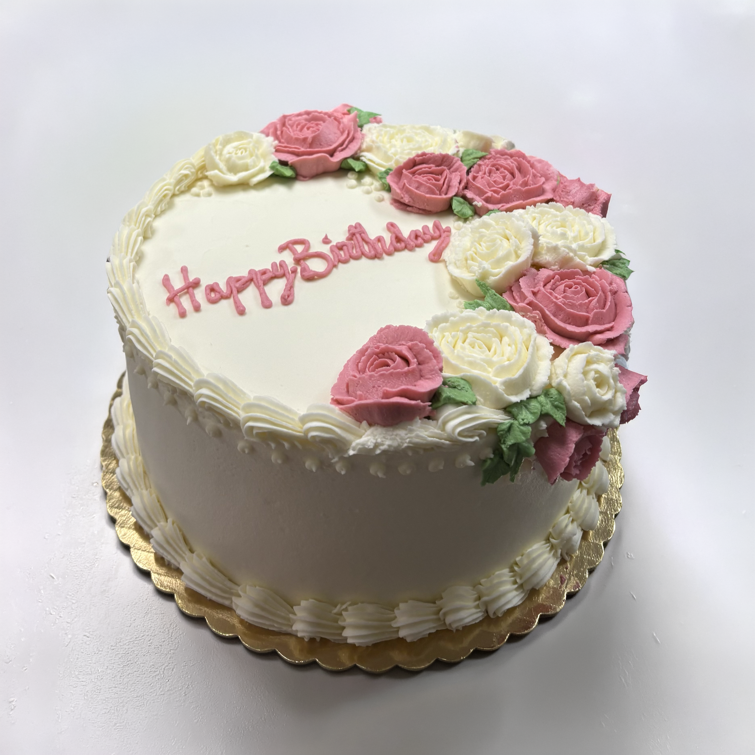Decorated birthday cake with pink and white buttercream roses, green leaves, and a pink "Happy Birthday" message.