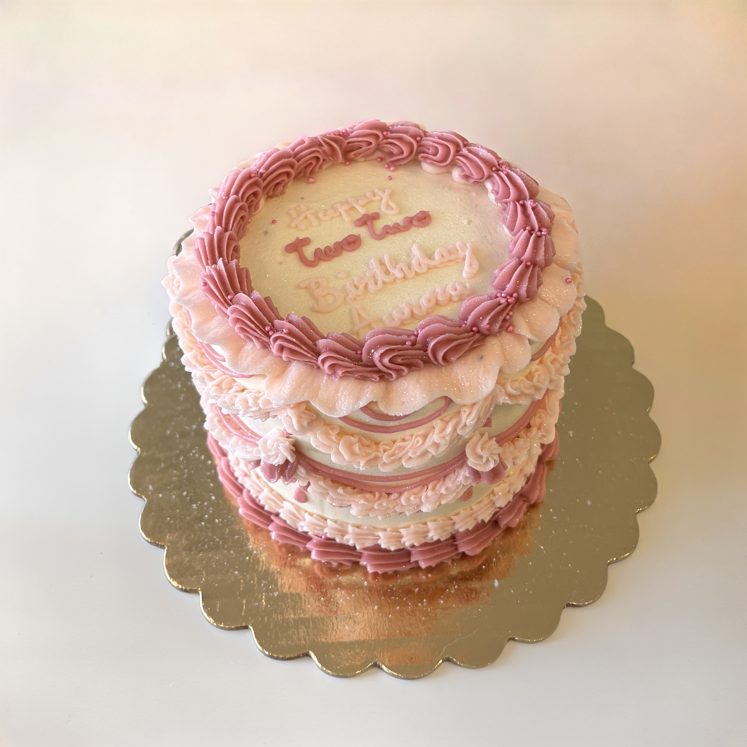 A round birthday cake decorated with pink frosting and pink sprinkles, with a message written in pink icing on top.