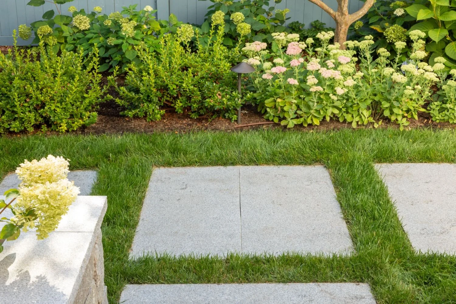 Custom stone retaining wall detail supporting raised patio in Newton, MA