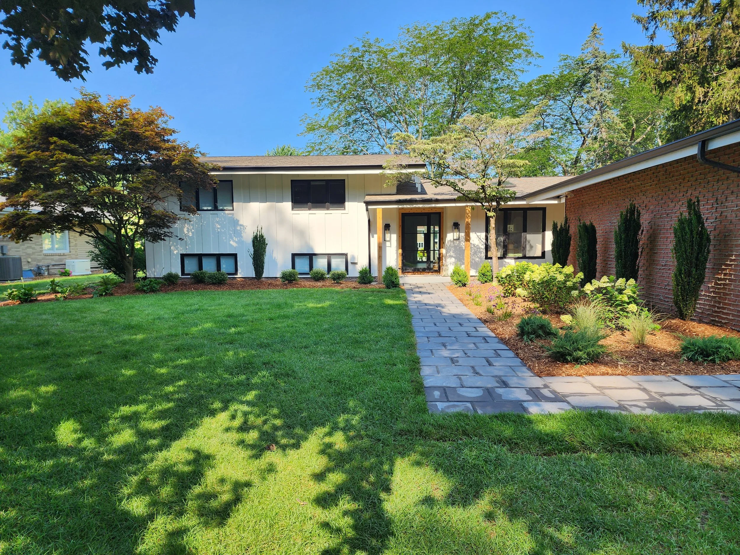 Front view of a modern house with a landscaped yard, brick pathway, and trees.