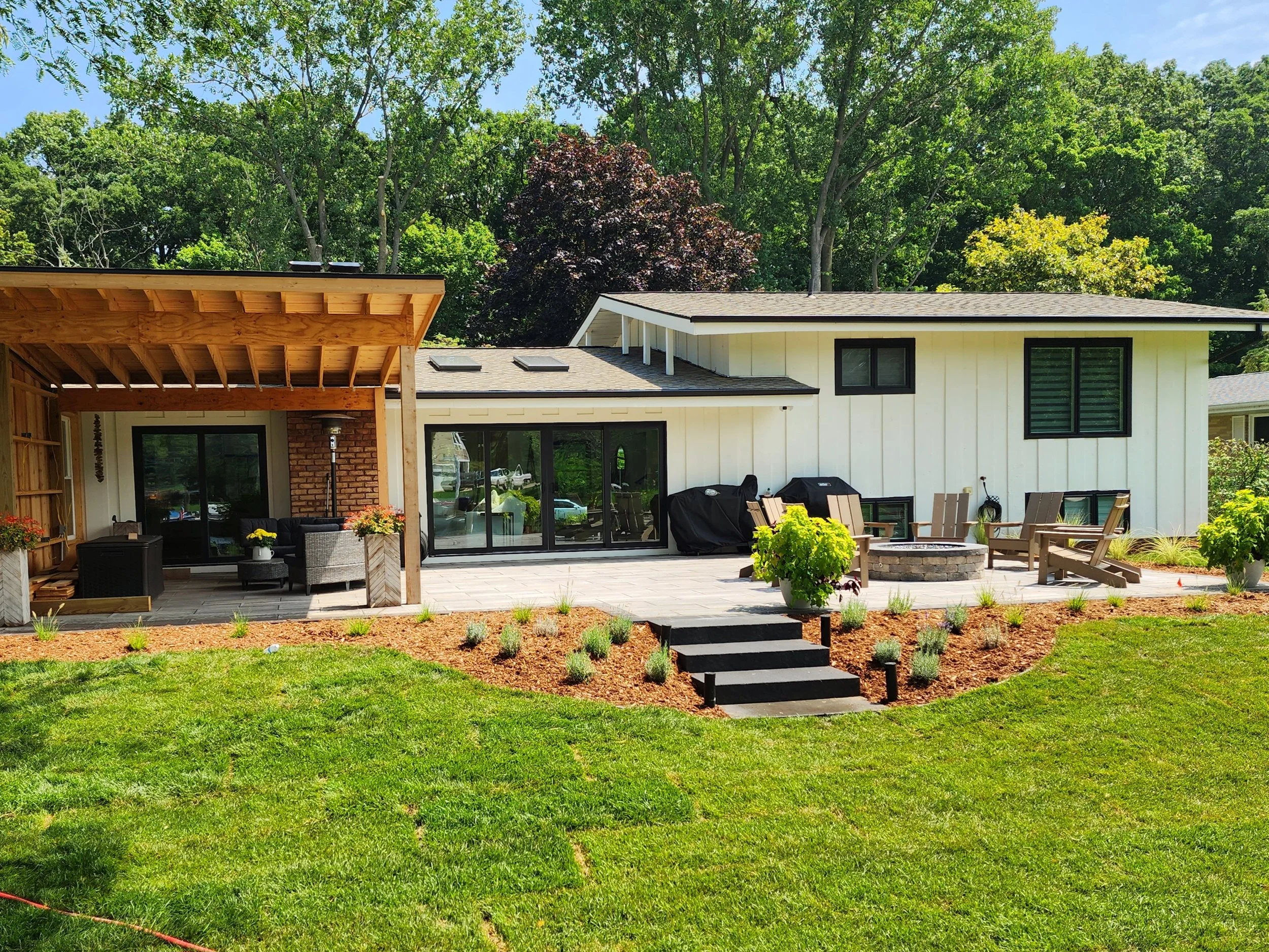Backyard with a patio, seating area, fire pit, and lawn, surrounded by trees.