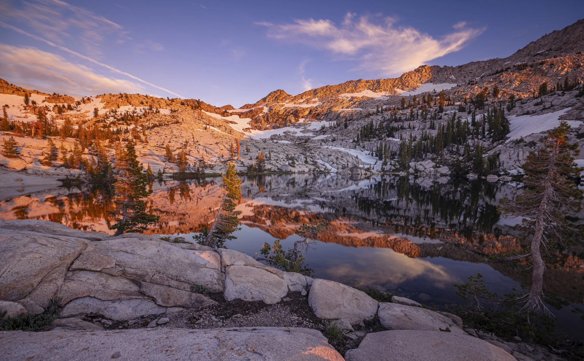 A mountain lake reflecting snow-capped peaks and pine trees during sunset
