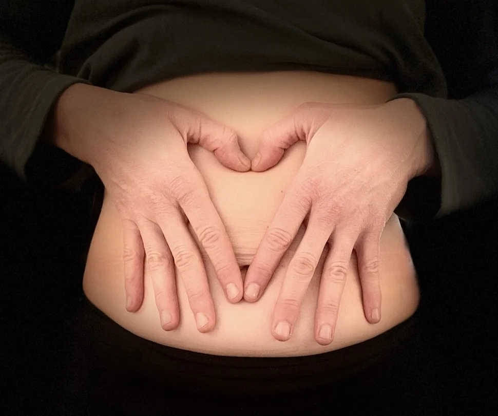 This is a photograph of hands in the shape of a heart on an exposed abdomen.