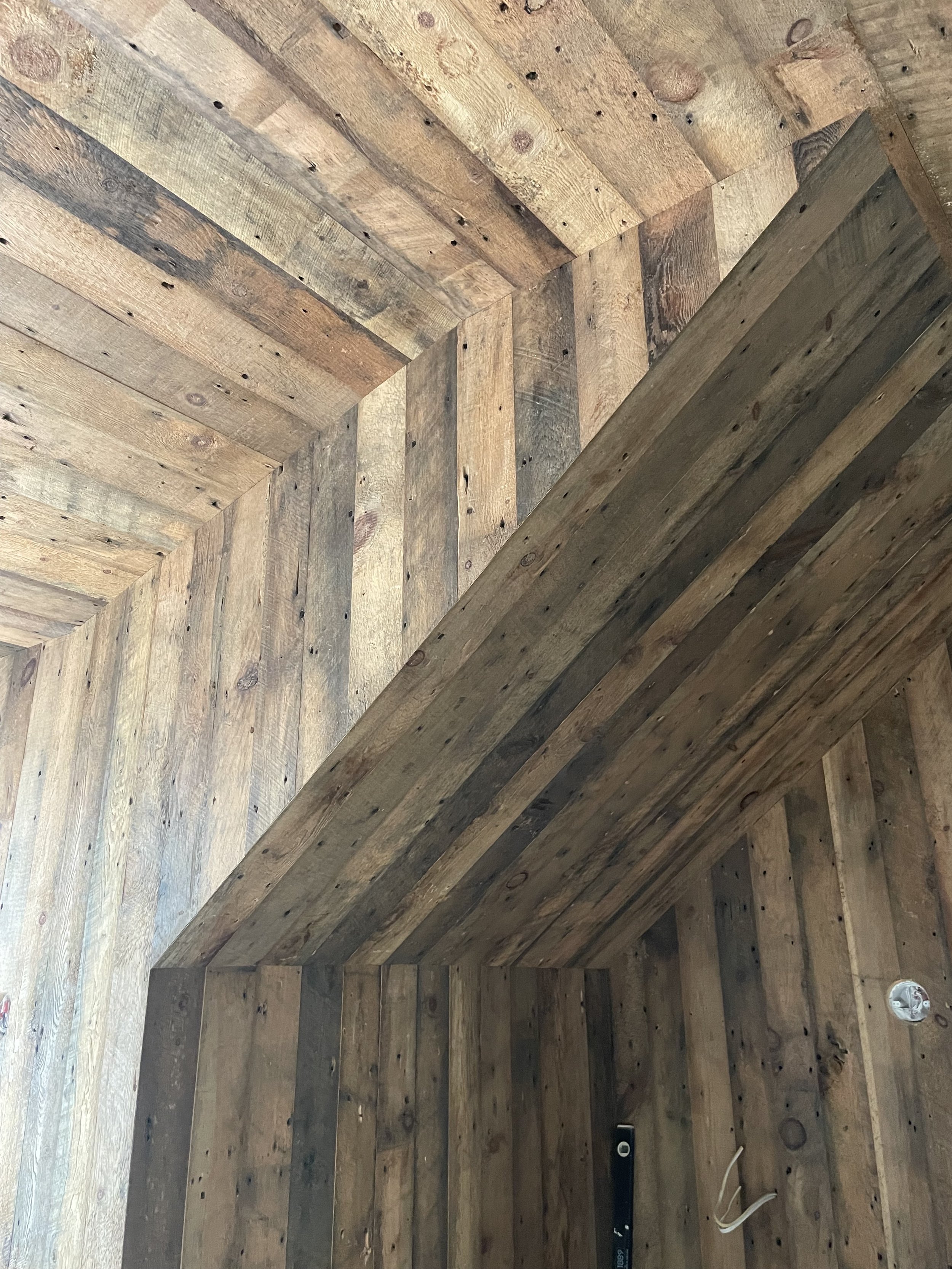 The image shows a wooden structure, possibly a wall or ceiling, made of horizontally arranged planks with visible textures and knots. The wood appears to be weathered and untreated.