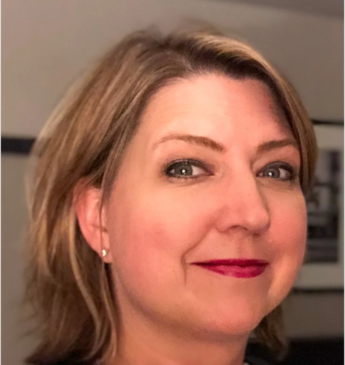 Close-up of a woman with blonde hair, fair skin, blue eyes, wearing makeup, a pearl necklace, and earrings.