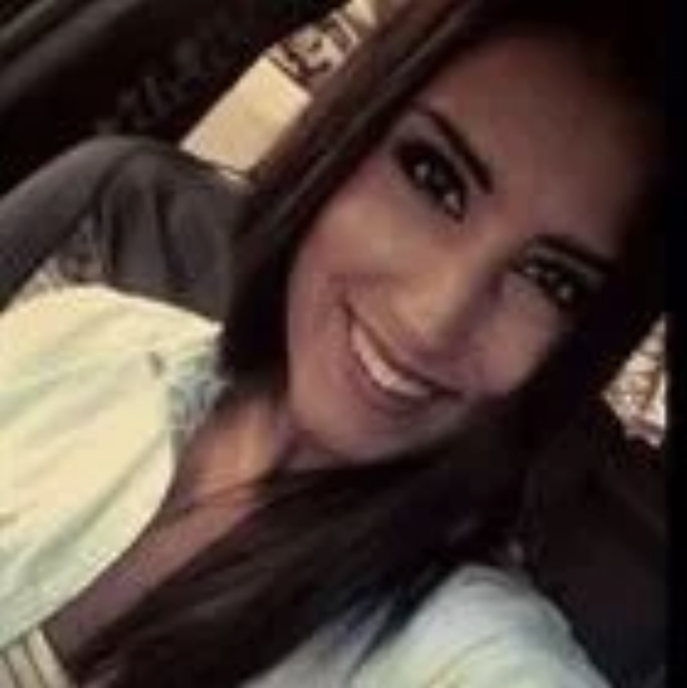 A woman smiling with long dark hair, wearing a light-colored top.