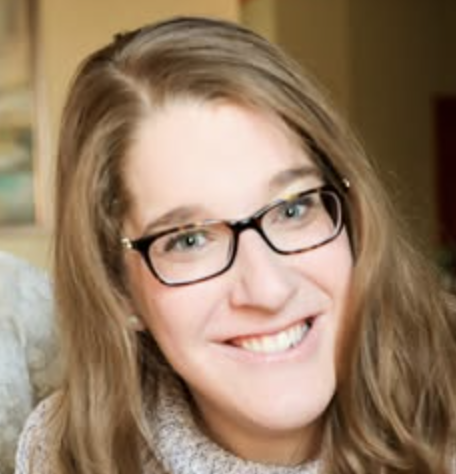 Close-up of a young woman with long brown hair, glasses, and a big smile.