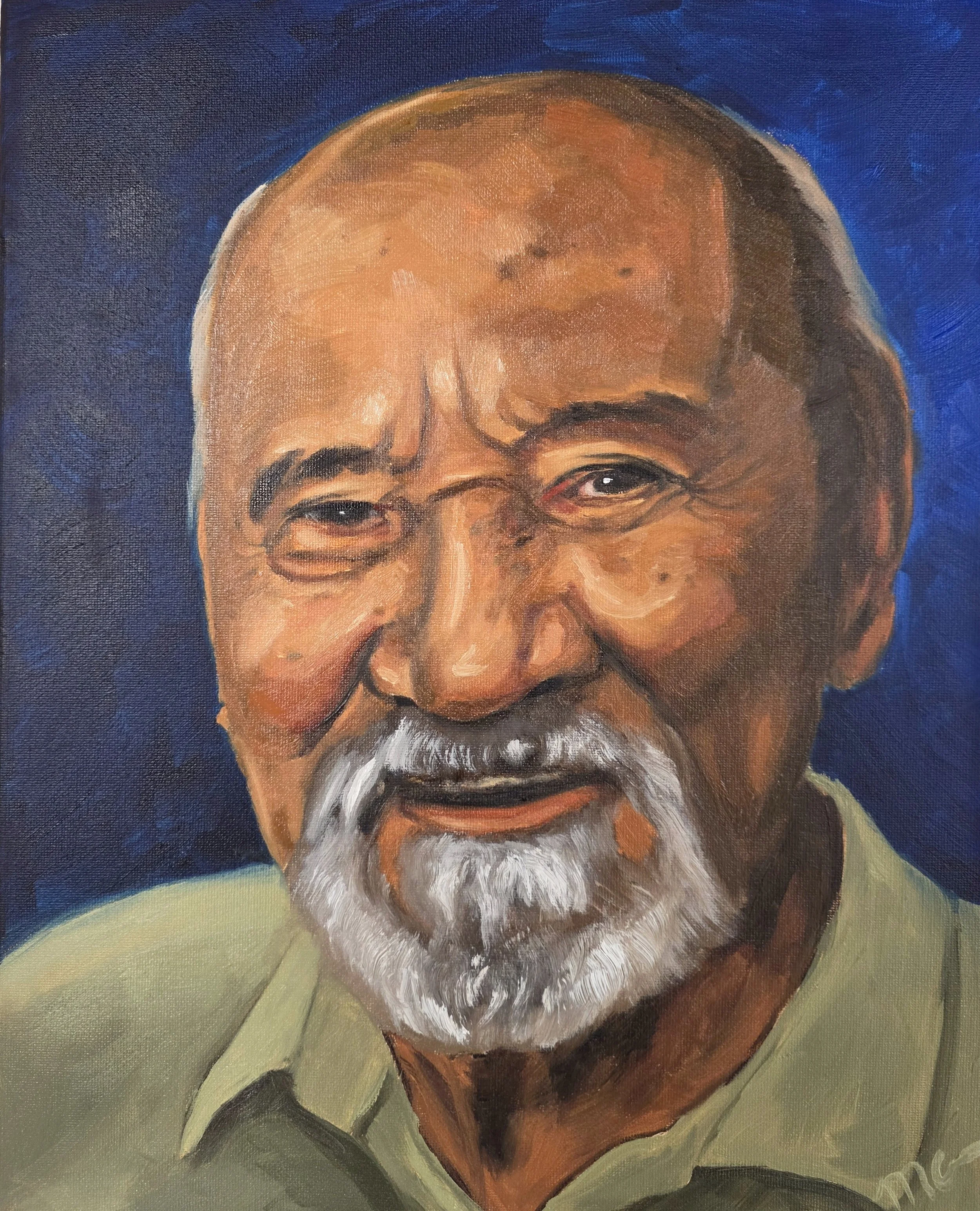 Portrait of an elderly man with a bald head, glasses, a white beard, wearing a light-colored shirt, smiling against a blue background.