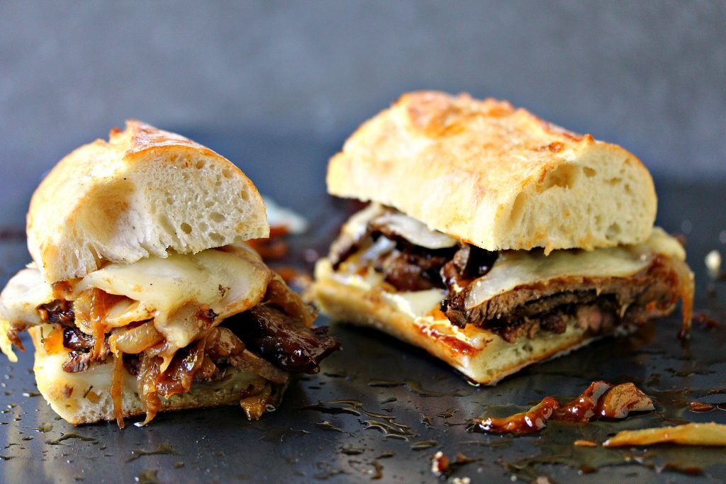 Gourmet steak sandwich with melted cheese and caramelized onions on a sliced baguette.