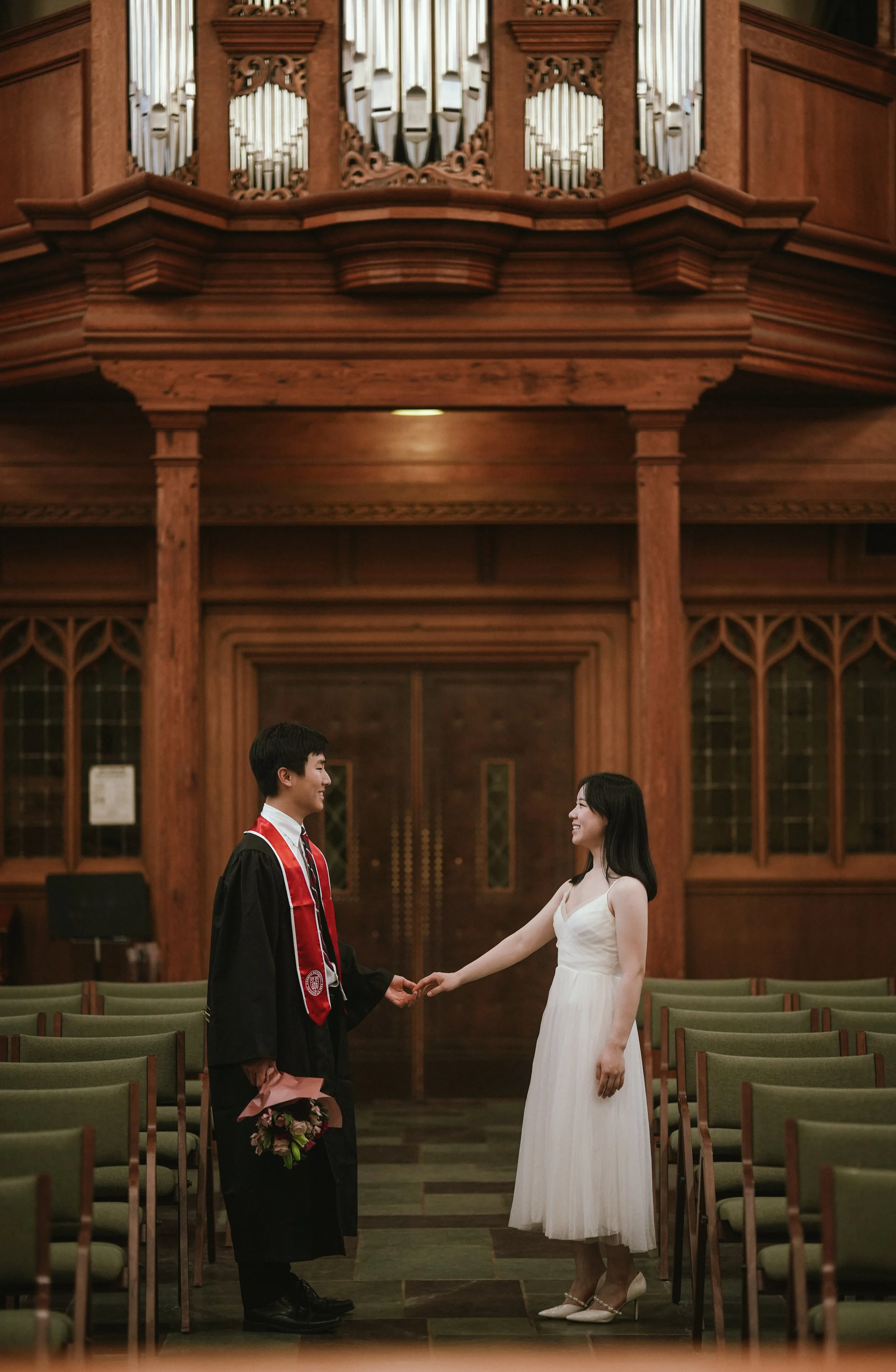 A bride and groom standing inside a wooden church, holding hands and smiling at each other during their wedding ceremony.