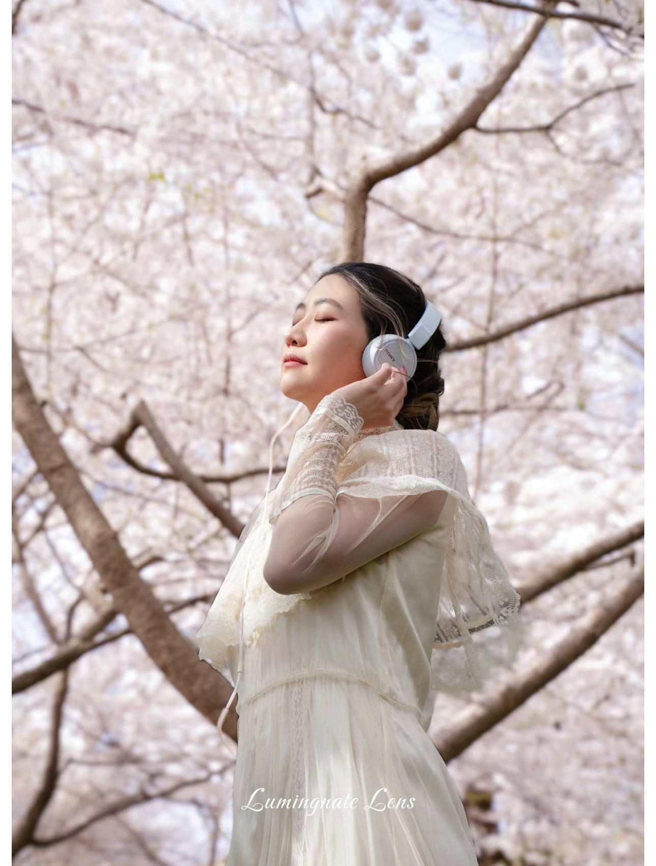 Woman in vintage dress with headphones in cherry blossom setting
