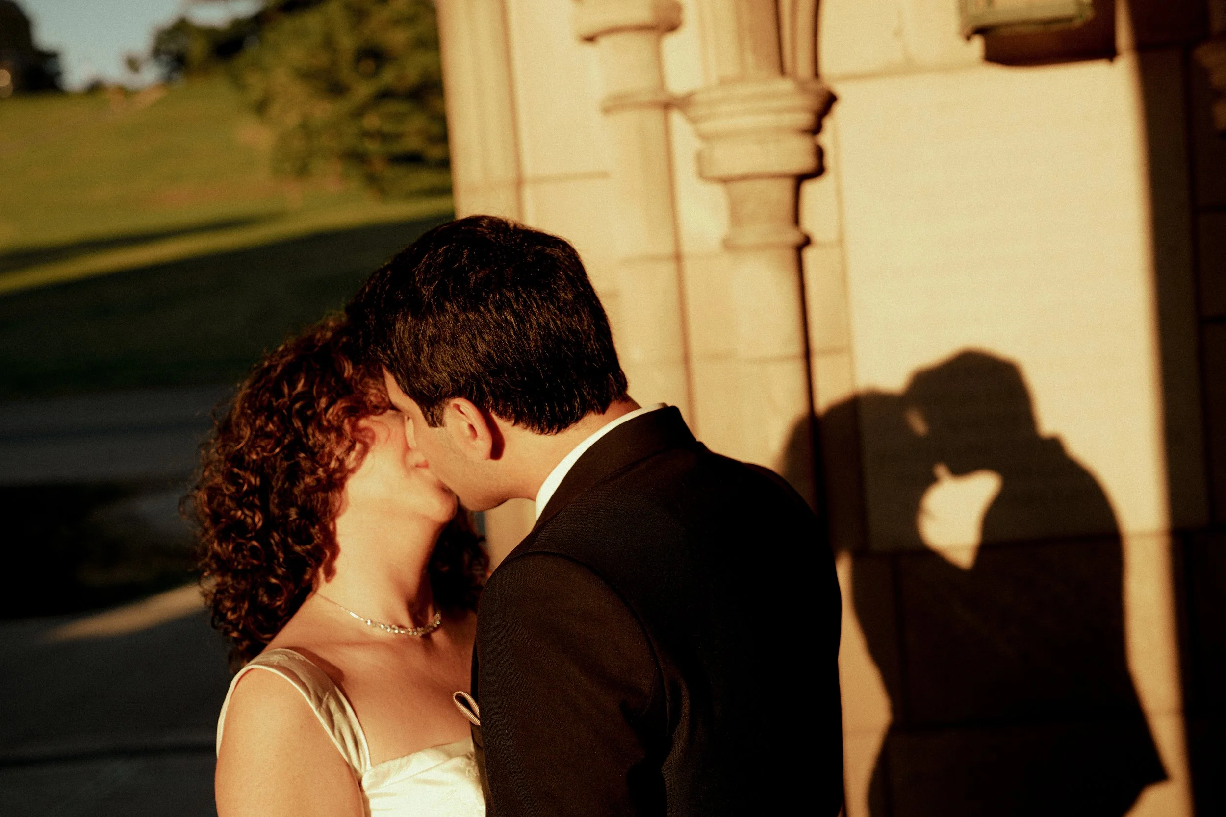 A couple shares a kiss during their wedding ceremony, with the bride in a white dress and the groom in a black tuxedo, standing close together.