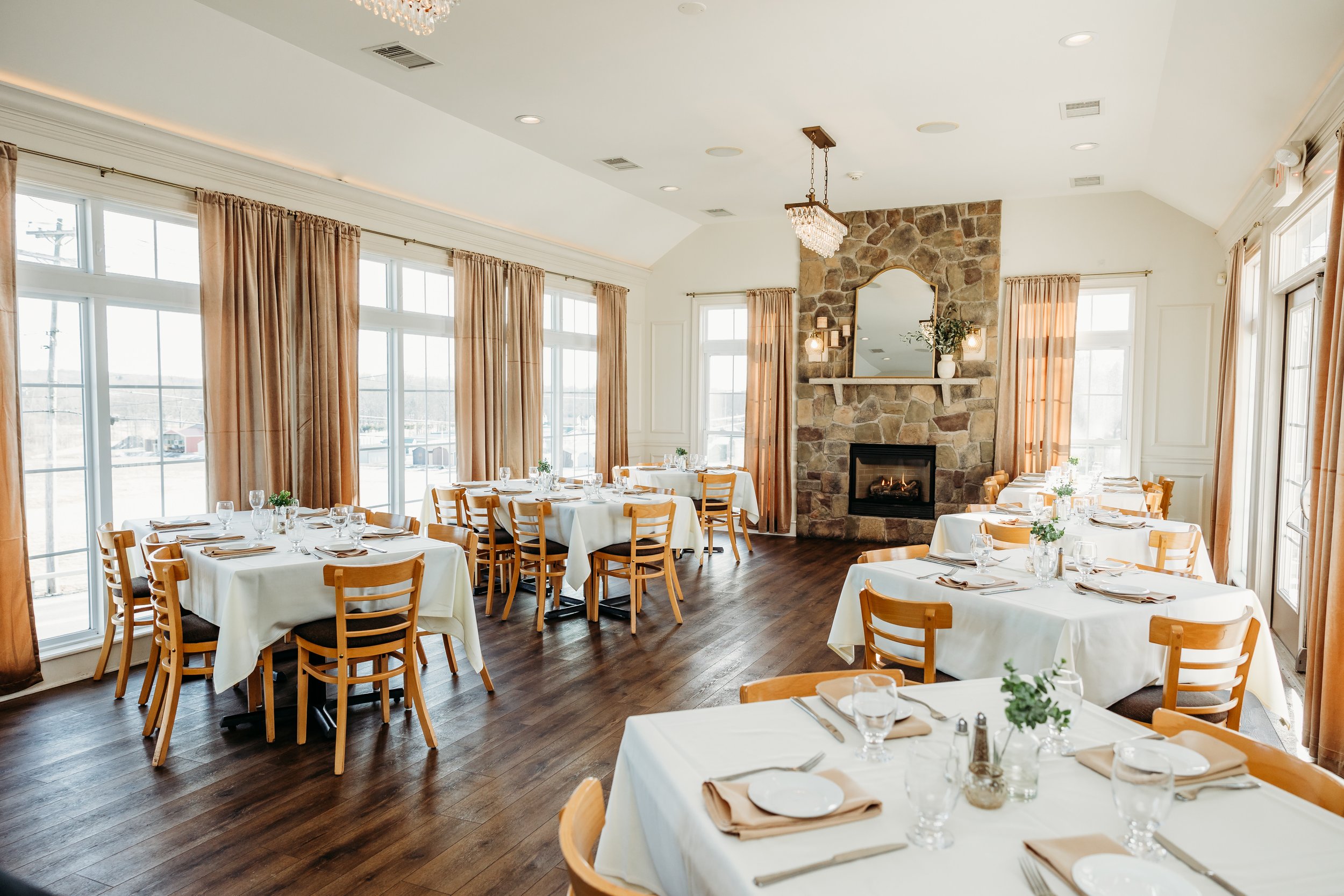 Elegant restaurant interior with wooden chairs, white tablecloths, and a stone fireplace