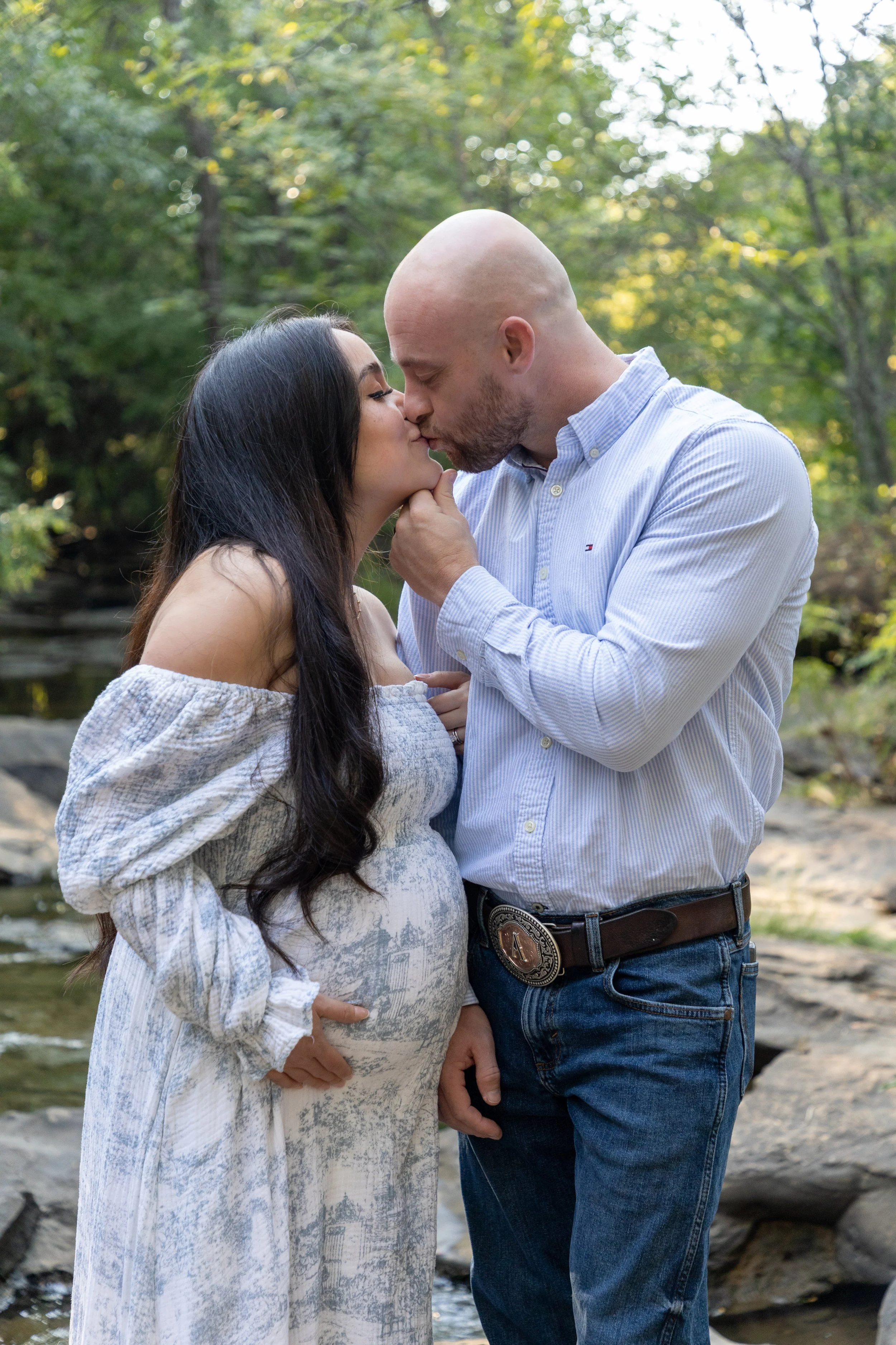 A couple sharing a kiss by a creek in a wooded area.