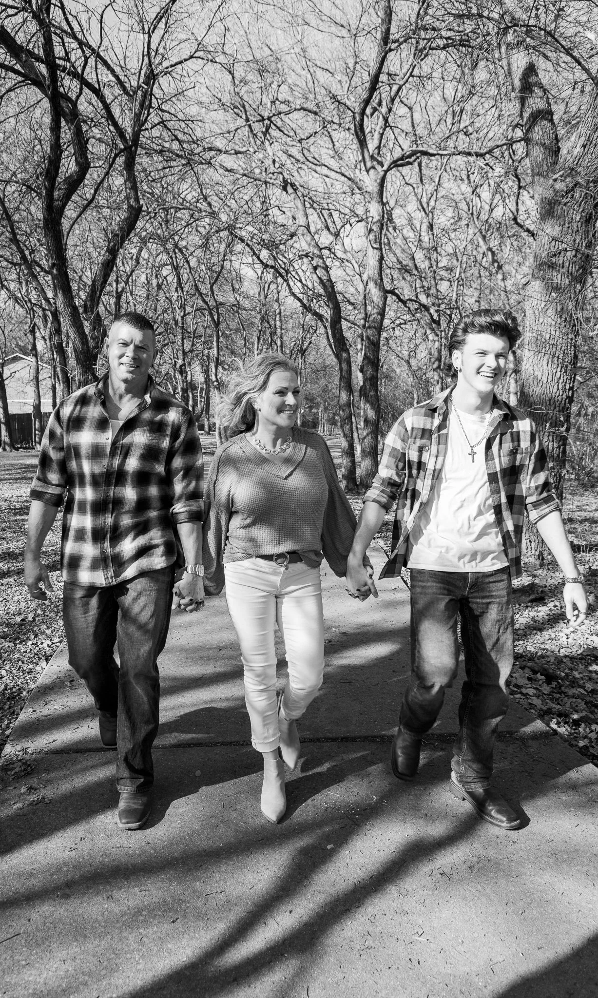 A black and white photo of a group of three people walking hand in hand on a paved path in a park with leafless trees in the background.