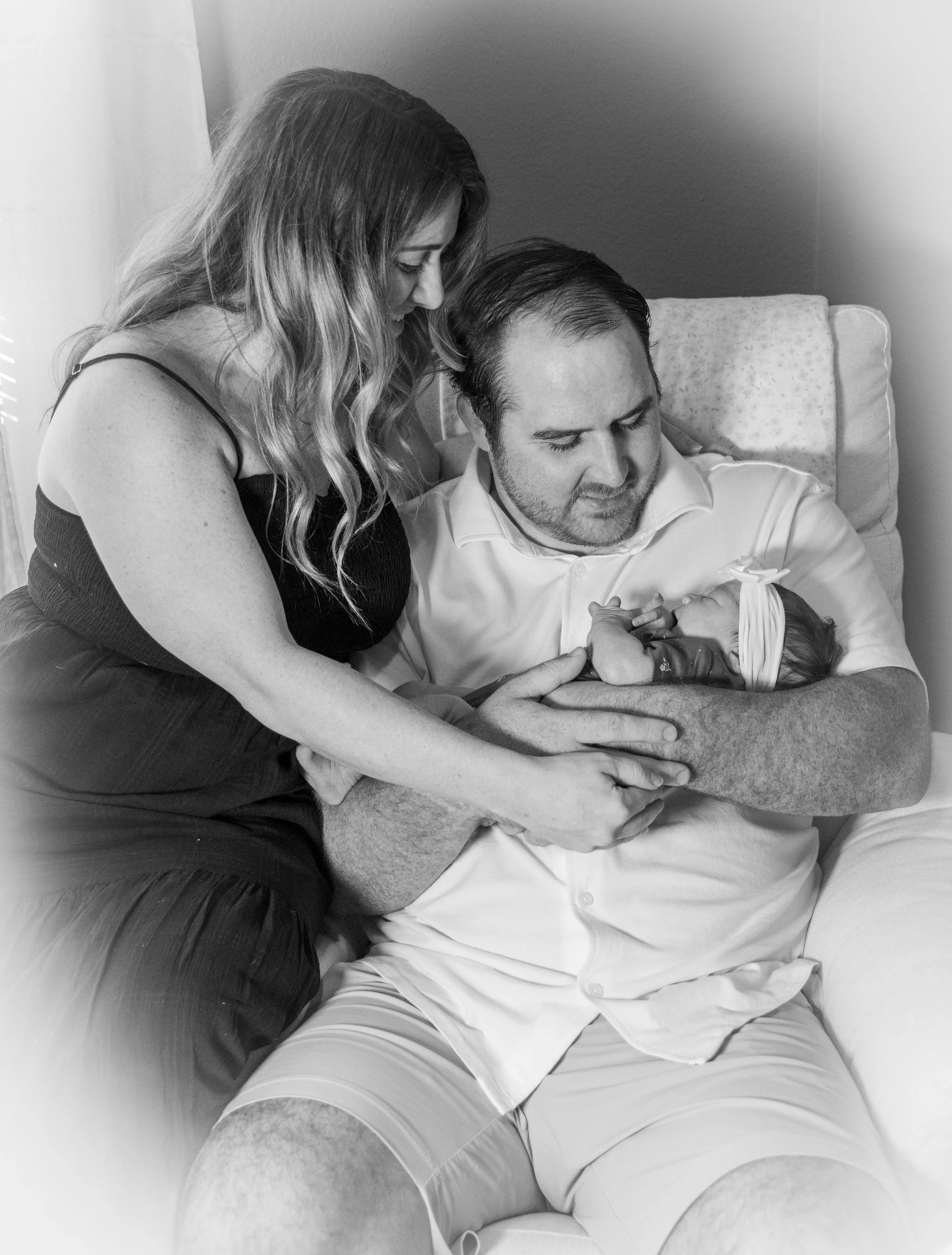 A woman and a man are sitting closely together, with the woman leaning over the man. They appear to be holding hands and possibly recovering in a hospital or medical setting, based on the man's clothing and bed.